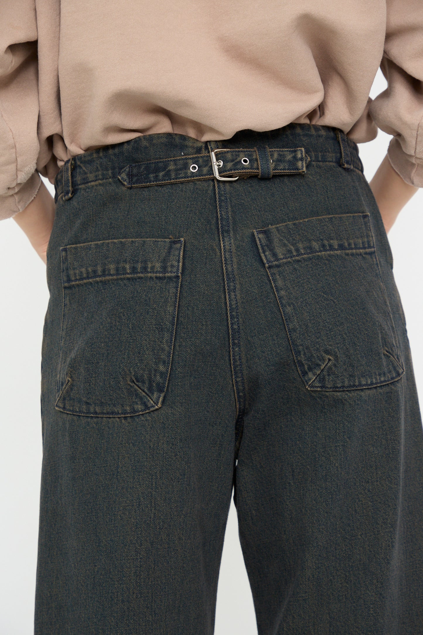 A person is seen from the back wearing Rachel Comey's Handy Pant in Brown, featuring high-waisted, relaxed fit Japanese denim with visible back pockets and a belt, paired with a beige shirt.