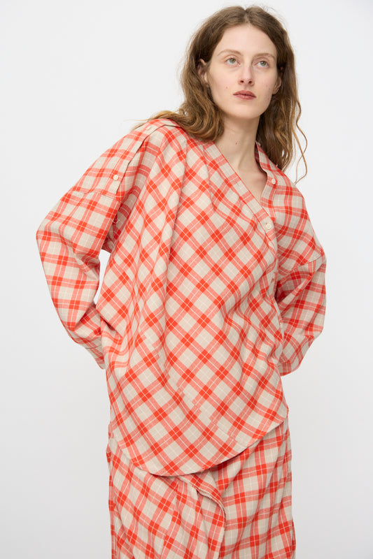 A woman with long brown hair wears the Rachel Comey Hollow Top in Red, a loose-fitting plaid cotton flannel with button detail, paired with a matching skirt, standing against a plain white background.