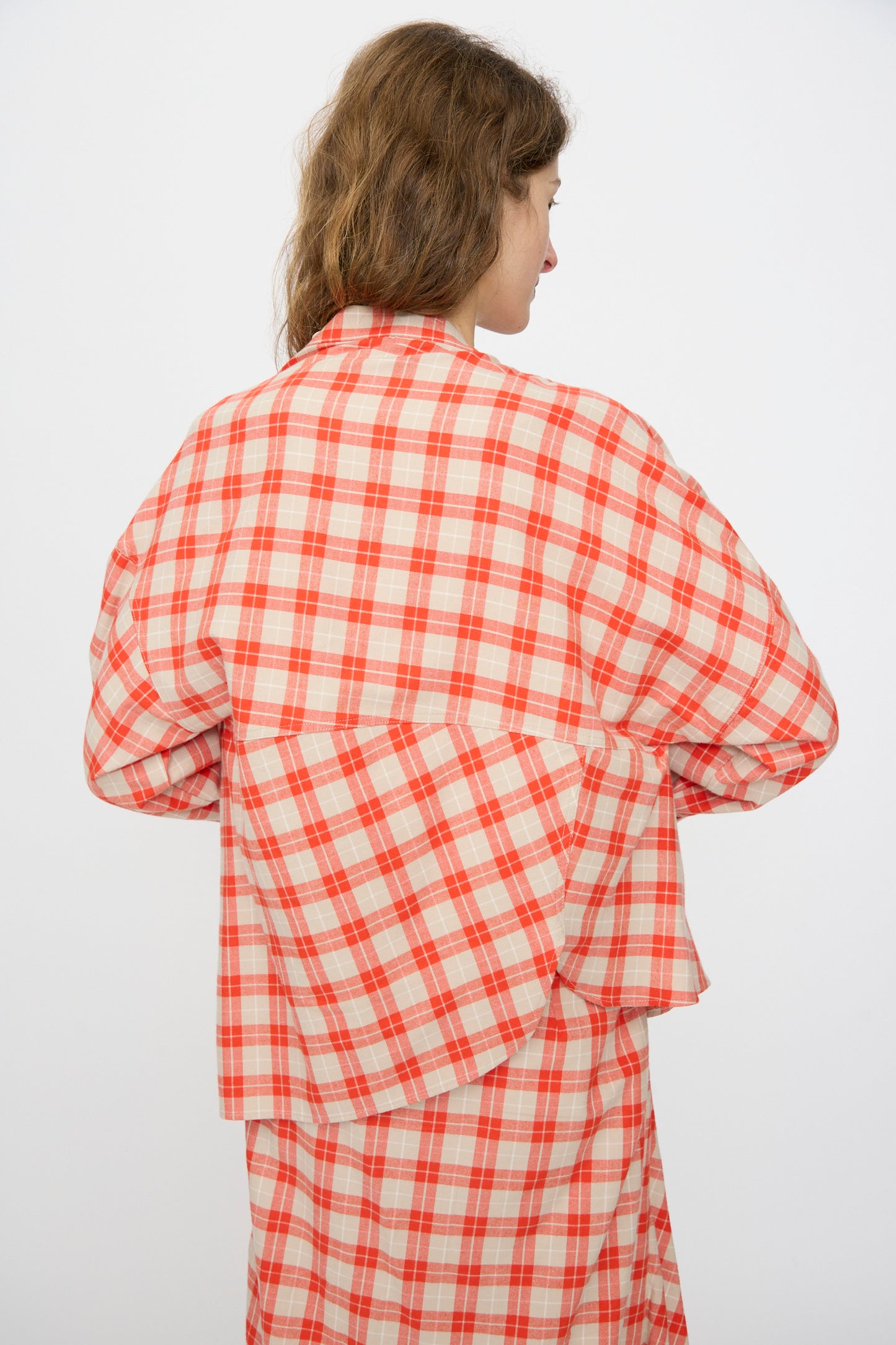 A person with light brown hair wears the Rachel Comey Hollow Top in Red, a cotton flannel shirt with an irregular, layered back design, standing against a plain white background.