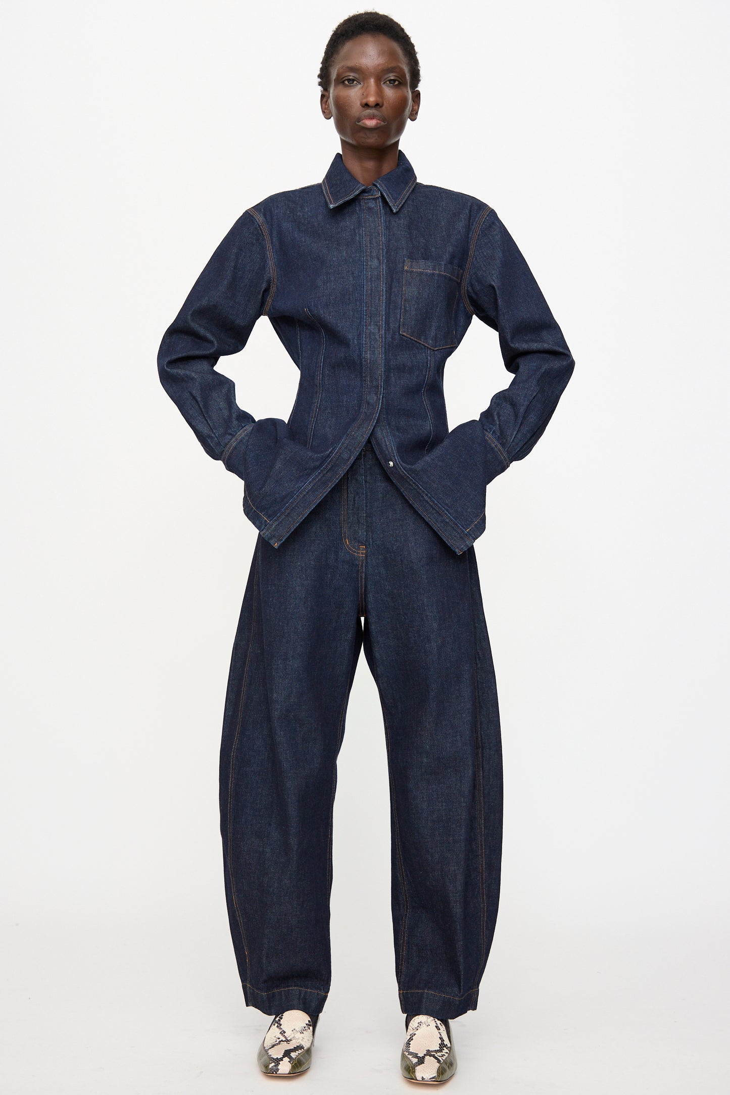 A person stands facing forward with hands in pockets, wearing Rachel Comey Keenan Pant in Raw Wash and light-colored snakeskin pattern shoes, set against a plain white background.