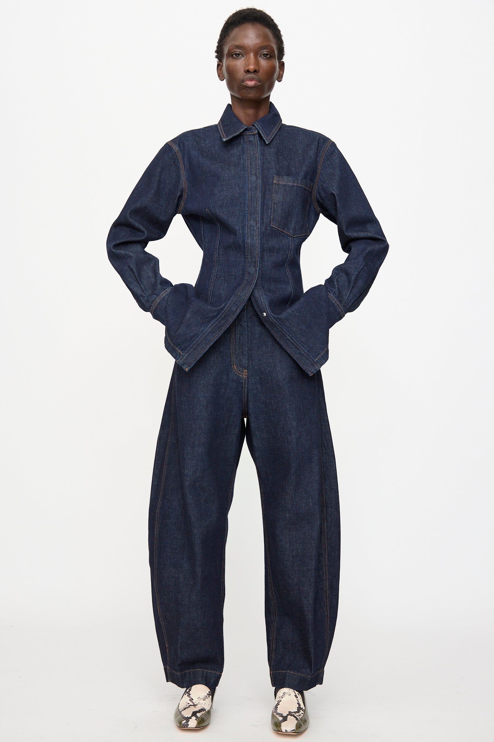 A person stands facing forward with hands in pockets, wearing Rachel Comey Keenan Pant in Raw Wash and light-colored snakeskin pattern shoes, set against a plain white background.
