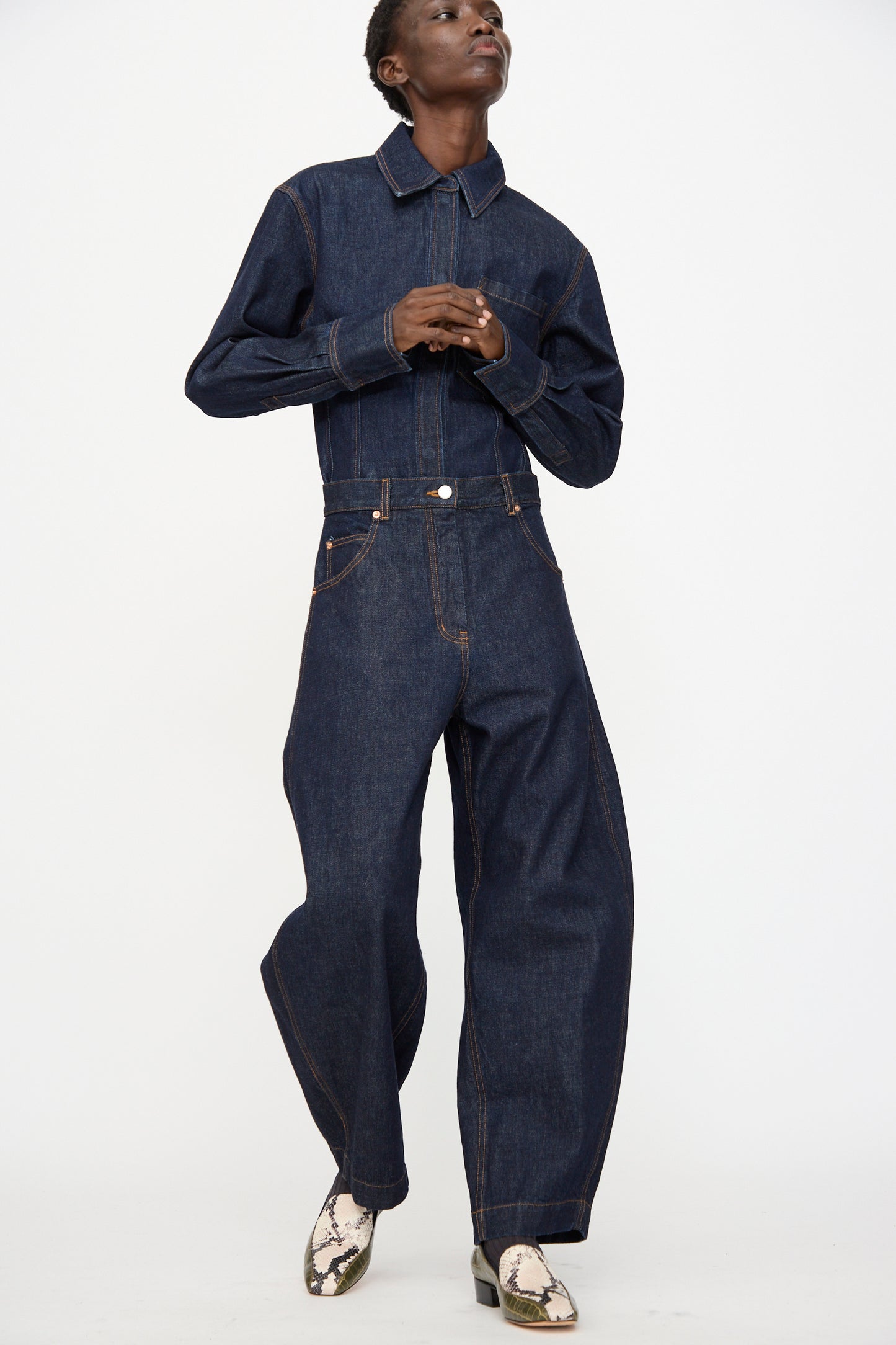 Person wearing the Rachel Comey Keenan Pant in Raw Wash, a dark high-waist wide-leg denim style, paired with snake-print boots and standing against a plain white background.