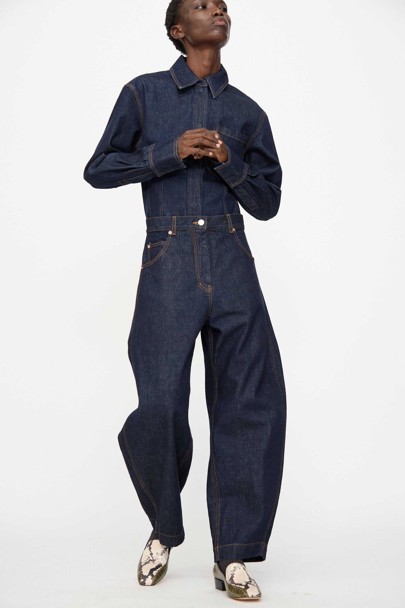 Person wearing the Rachel Comey Keenan Pant in Raw Wash, a dark high-waist wide-leg denim style, paired with snake-print boots and standing against a plain white background.