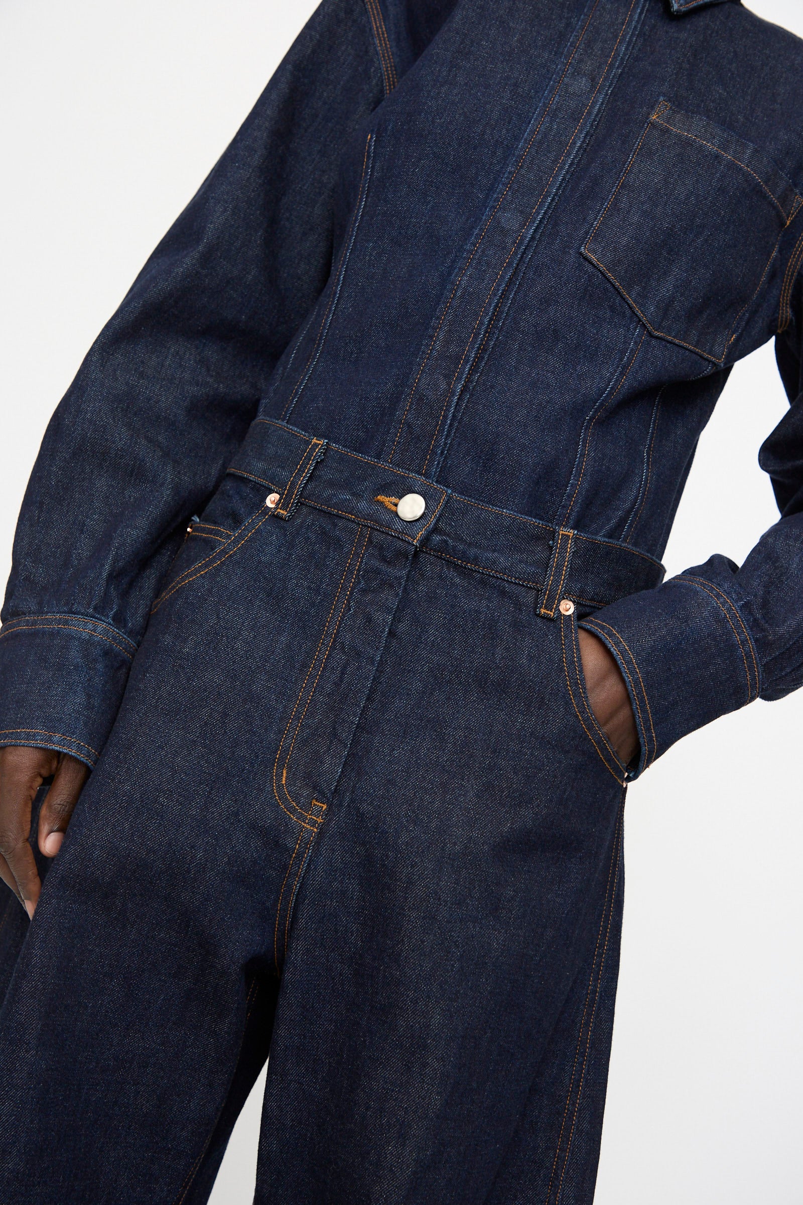 Model wears the Rachel Comey Keenan Pant in Raw Wash, a high-waisted dark blue denim style with visible orange stitching and one hand in the pocket, shown from neck to mid-thigh.