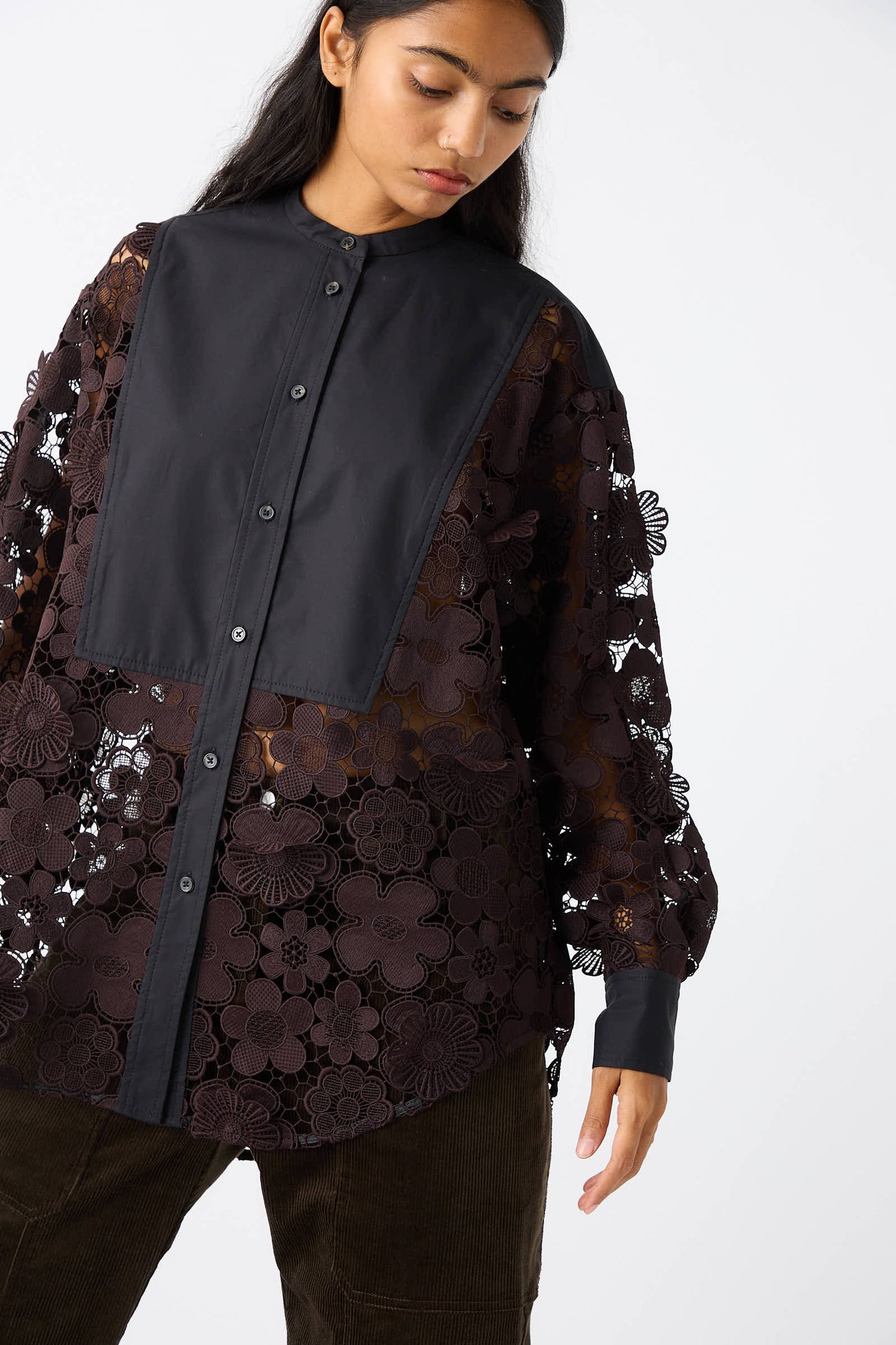 A person wearing a relaxed fit Lace Flower Myra Top in Dark Brown and Black by Rachel Comey stands against a plain white background.