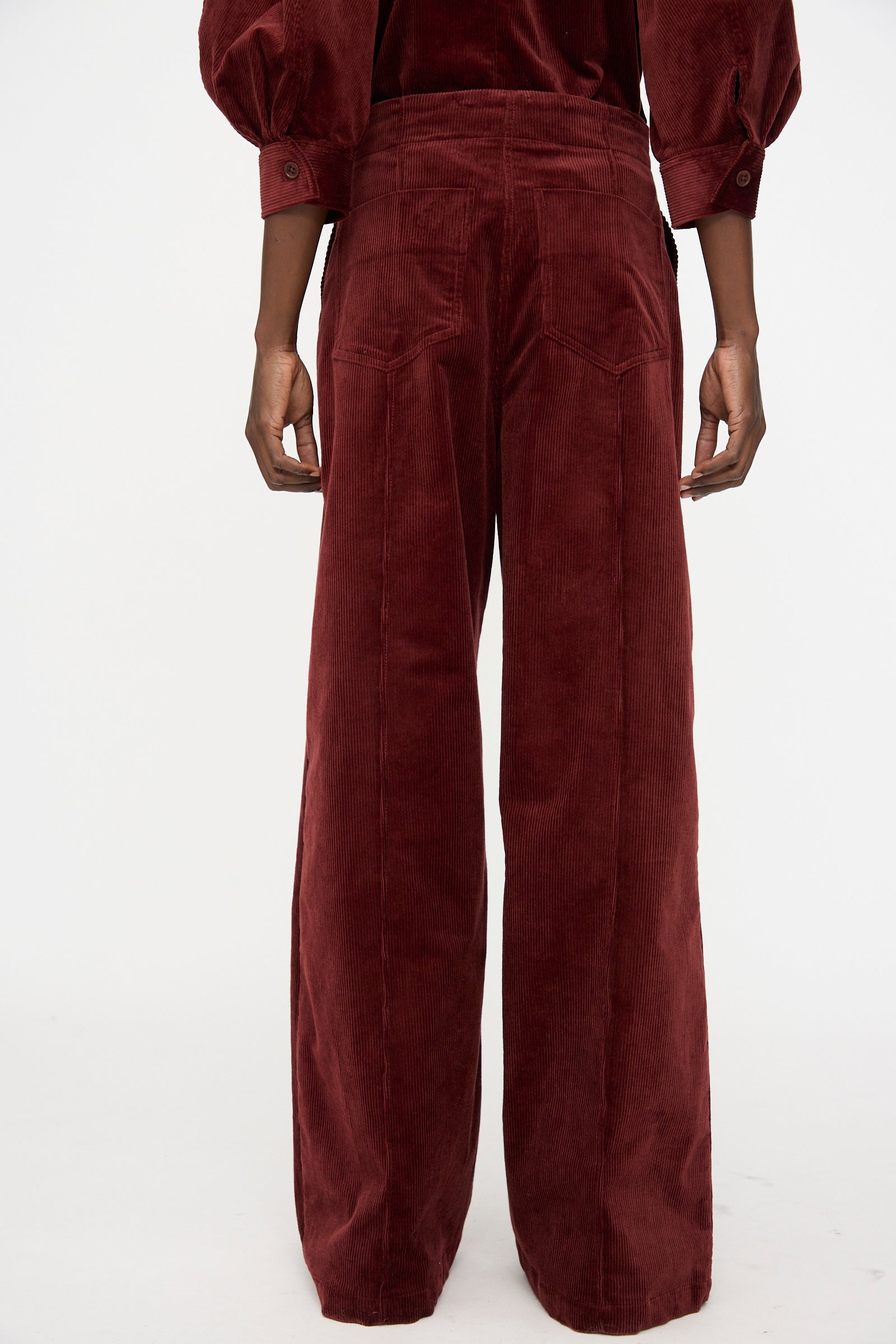 A person is shown from the back wearing Rachel Comey's Lanett Cord Pant in Brick, a high-waisted, wide-leg corduroy style paired with a matching long-sleeve top against a white background—ideal for lovers of women’s relaxed-fit retro pants.