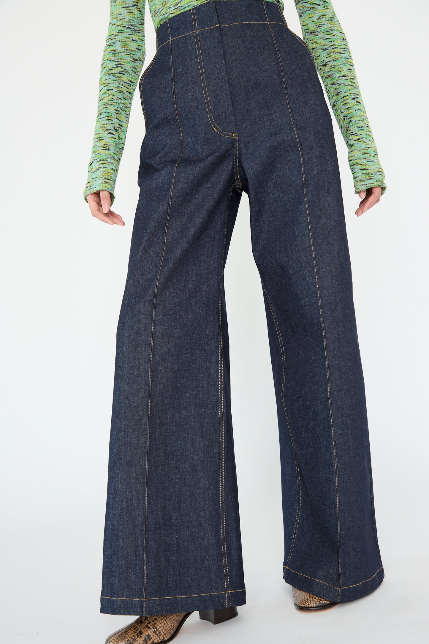 A model wears Rachel Comey's Lanett Pant in Super Raw, paired with a green and blue long-sleeve top and snake-print boots against a plain background.