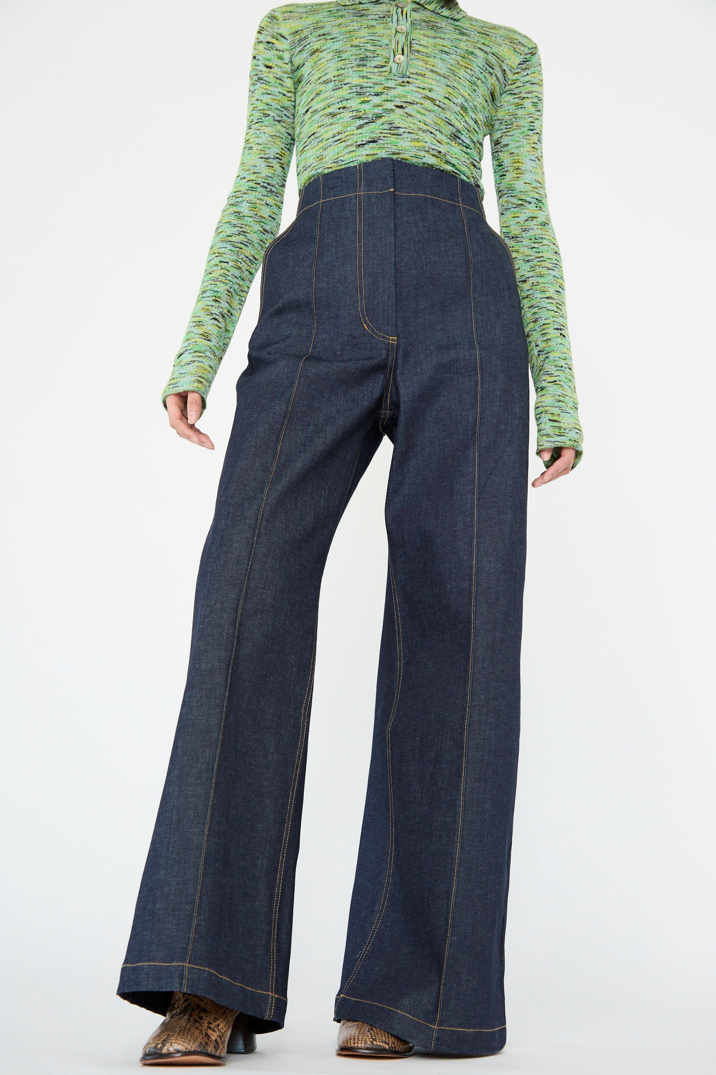 A person wears a green patterned long-sleeve top with Rachel Comey's Lanett Pant in Super Raw, paired with snakeskin boots against a white backdrop. 