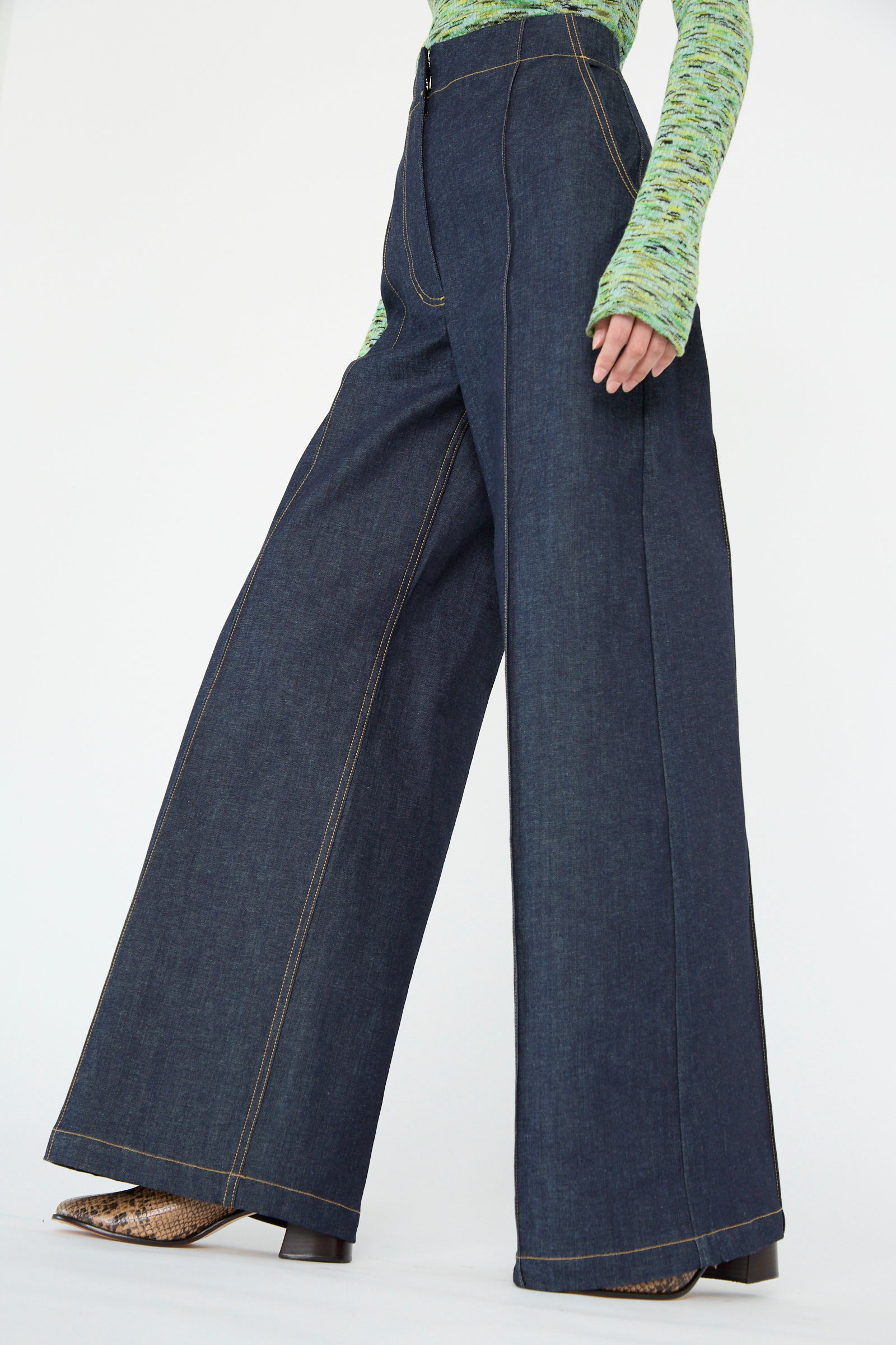 A model wearing Rachel Comey's Lanett Pant in Super Raw and a green textured top, seen from below the waist against a white backdrop. 