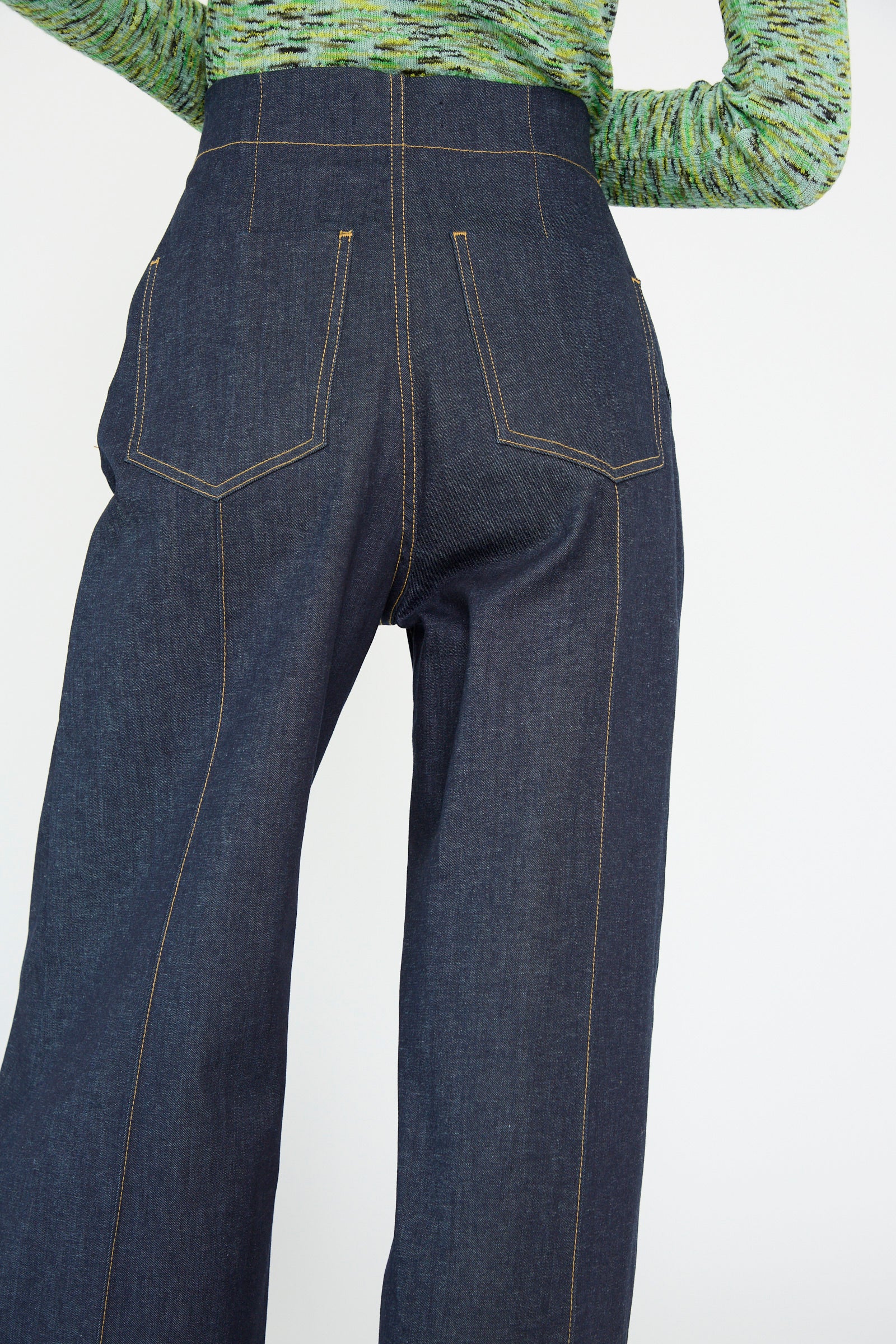 A person is seen from the back wearing Rachel Comey's Lanett Pant in Super Raw, which features dark blue high-waisted flared jeans, paired with a green textured top.