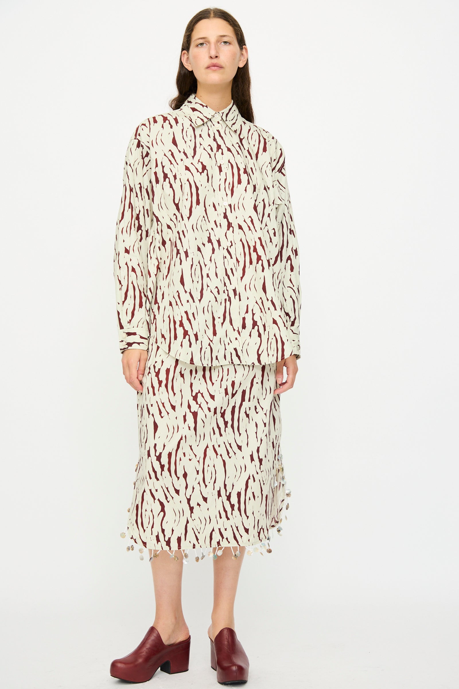 A person wears the Rachel Comey Lastica Skirt in Cream with a matching abstract pattern shirt and maroon closed-toe shoes, standing against a white background.