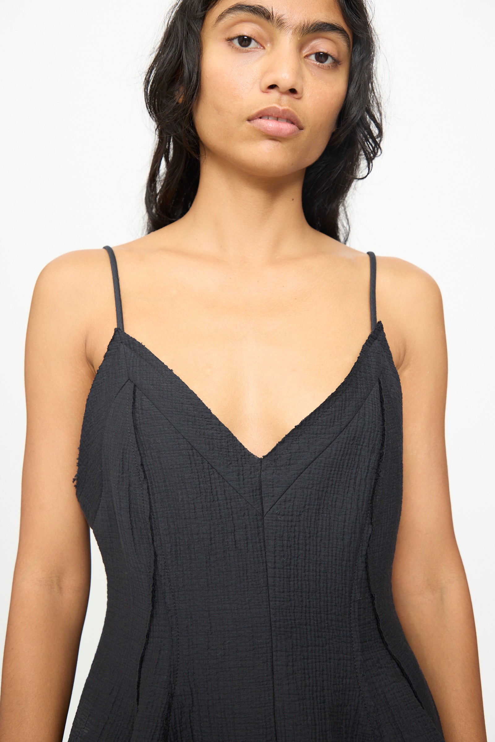 A person wearing the Rachel Comey Layley Top in Black, featuring a textured finish and spaghetti straps, stands against a plain white background, looking at the camera.