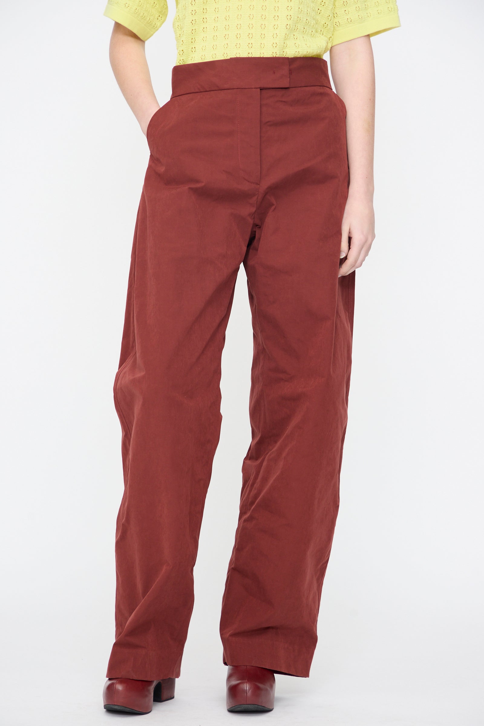 A person wearing a yellow short-sleeve top, Rachel Comey Lyson Pant in Garnet, and matching rust-colored shoes stands against a white background.