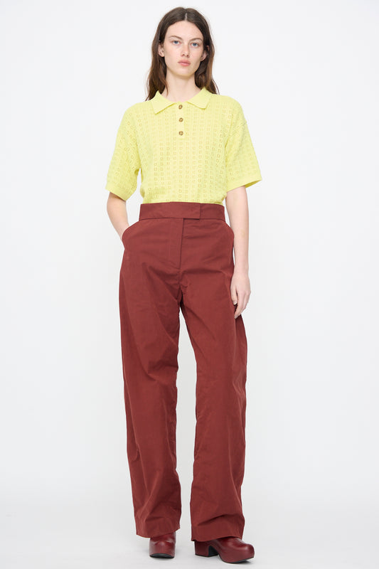 A person stands facing forward wearing a yellow short-sleeve button-up shirt, Rachel Comey Lyson Pant in Garnet, and maroon shoes against a plain white background.