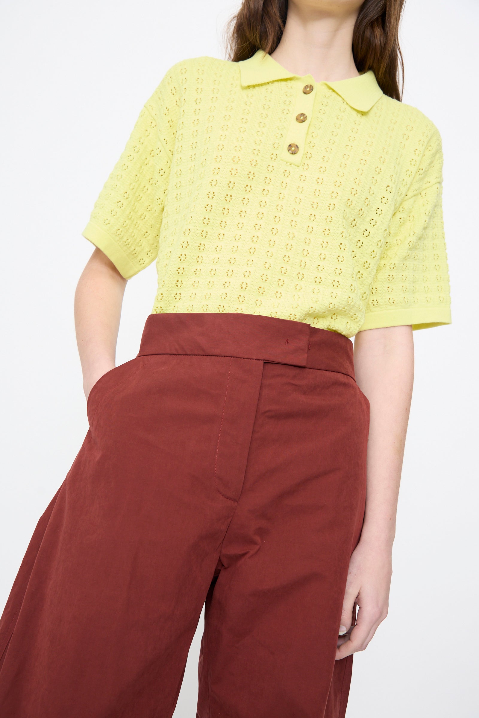 Person wearing a light yellow short-sleeve knit polo with brown buttons, paired with the Rachel Comey Lyson Pant in Garnet.
