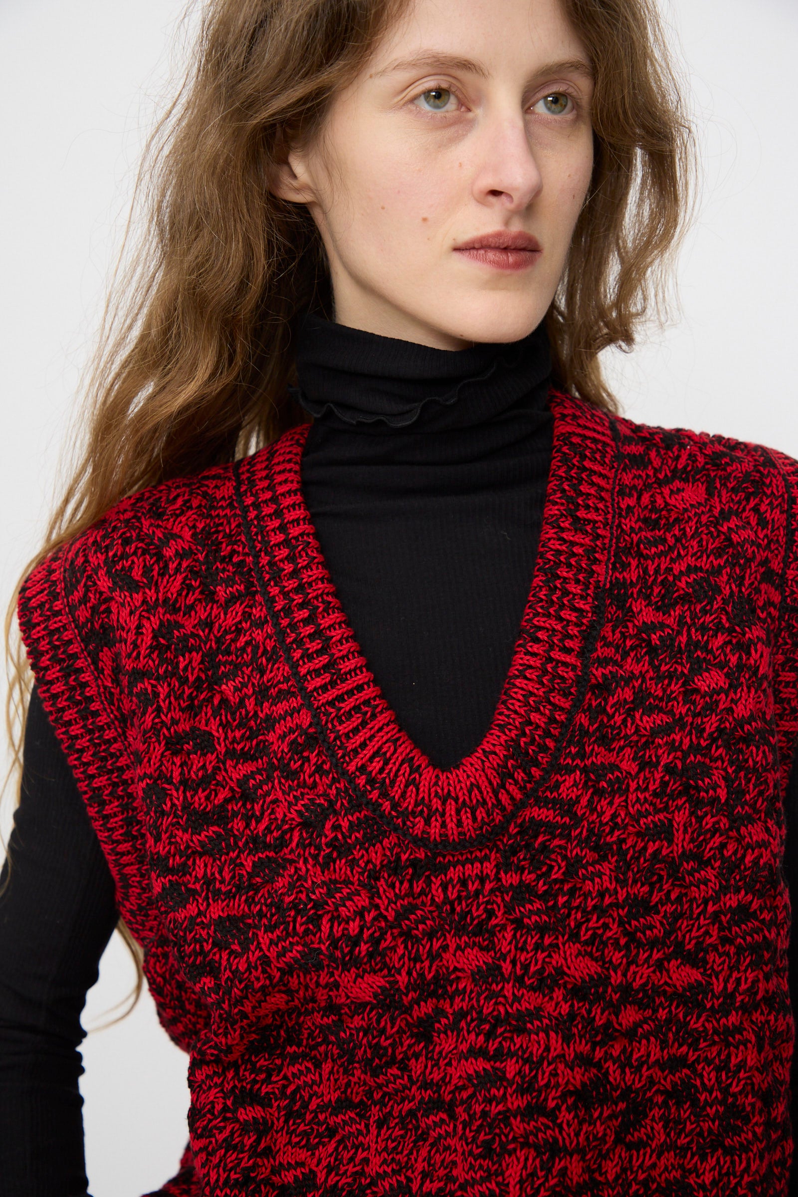 A woman with long brown hair wears the Rachel Comey Mati Vest in Red Marble over a black turtleneck.