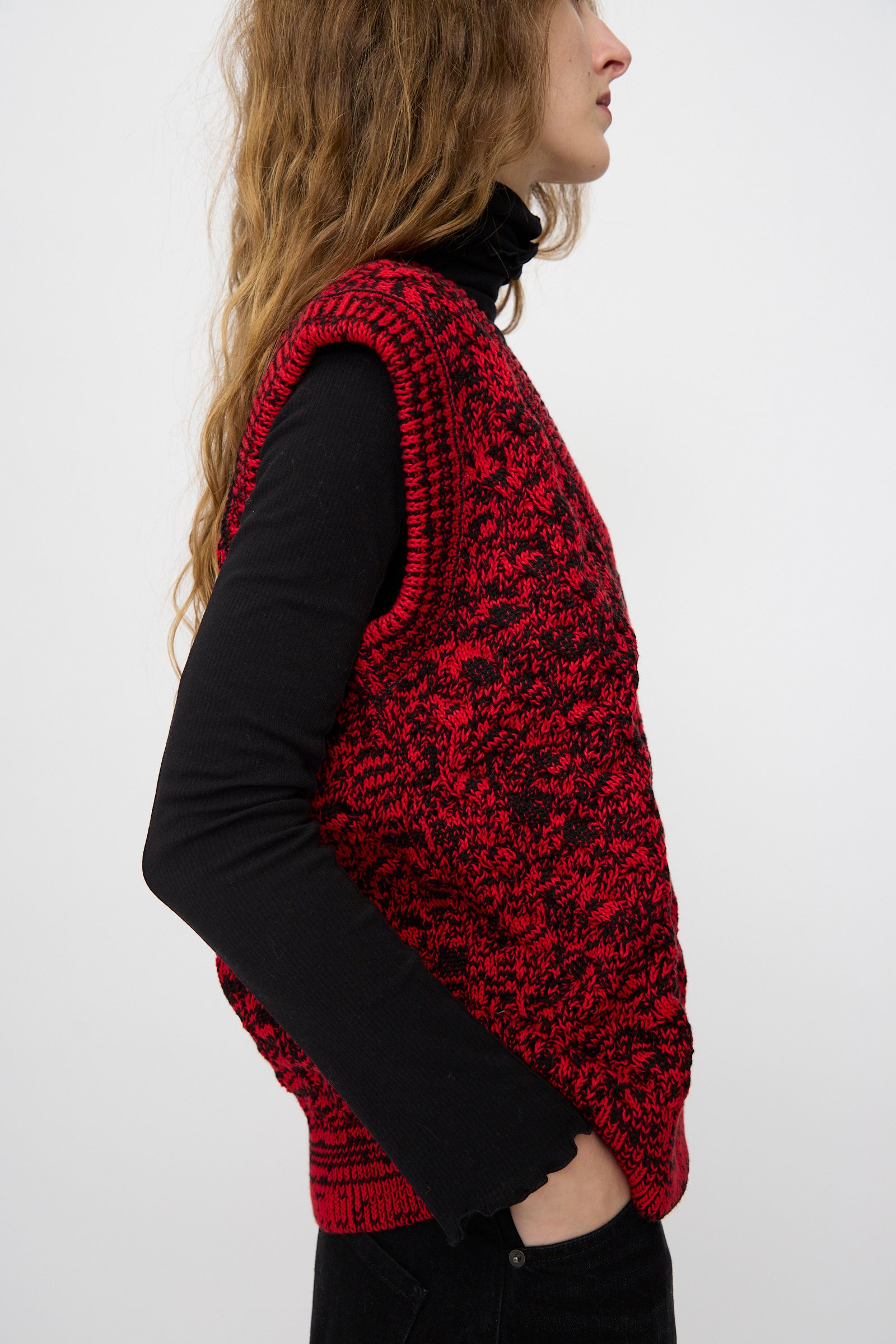 A person in a black turtleneck and pants wears the Rachel Comey Mati Vest in Red Marble, standing in profile against a plain light background.