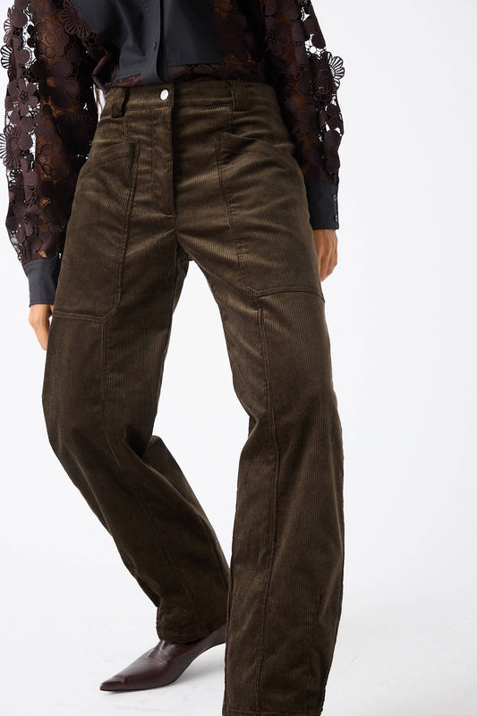 A person is modeling the Rachel Comey Mid Wale Corduroy Oberlin Pant in Bark, featuring relaxed fit, wide legs, and a high waist. They are also wearing a black lace sleeve top and brown pointed shoes.