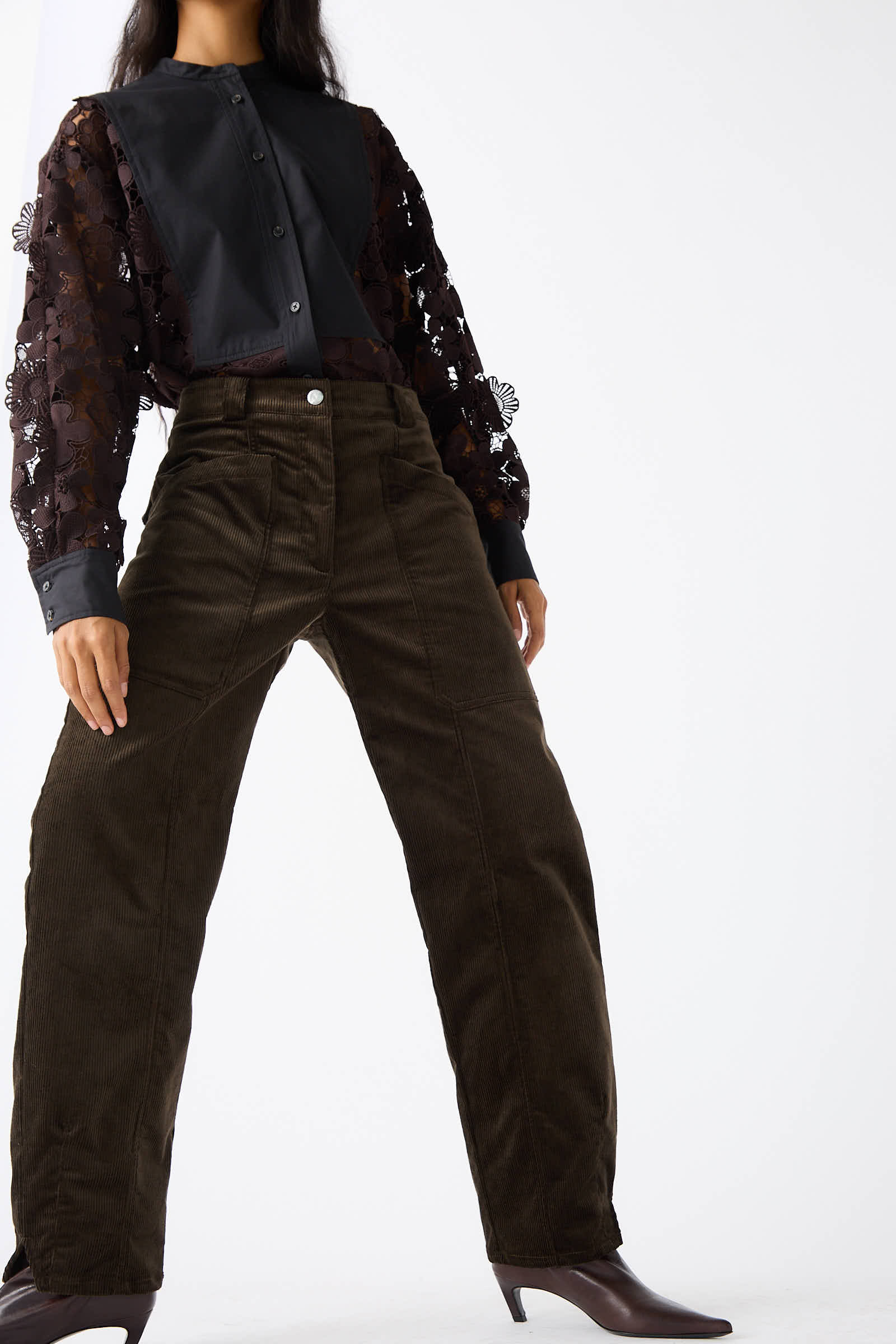 Person wearing a black blouse with sheer, floral-patterned sleeves and Rachel Comey Mid Wale Corduroy Oberlin Pant in Bark, standing in a confident pose against a plain background.