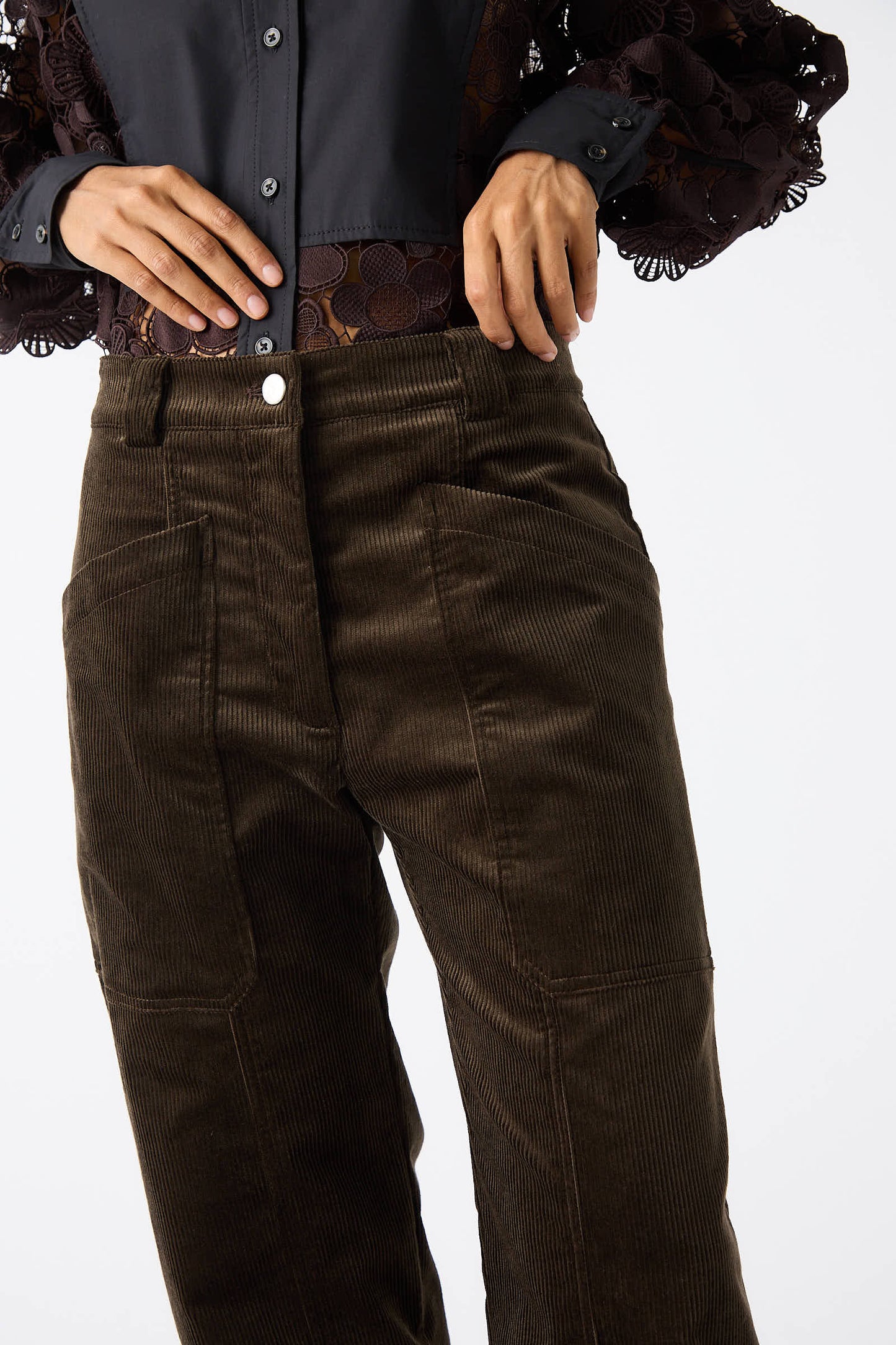 A person wearing a black shirt with lace sleeves is adjusting their high-waisted, relaxed fit, Rachel Comey Mid Wale Corduroy Oberlin Pant in Bark.