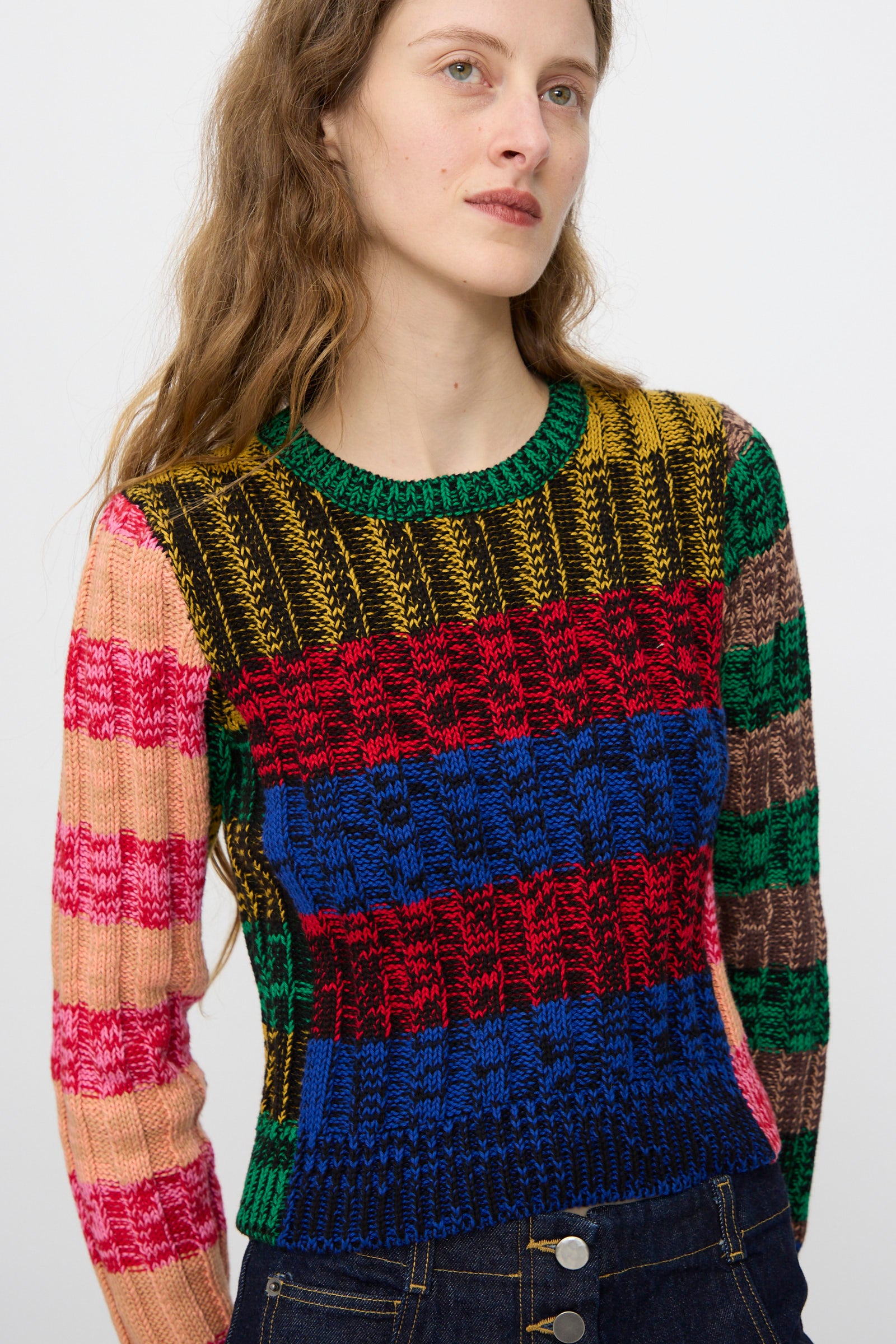 A person with long brown hair wears the Rachel Comey Muna Pullover in Stripe Multi, a cropped, colorful knit sweater, paired with dark high-waisted jeans.
