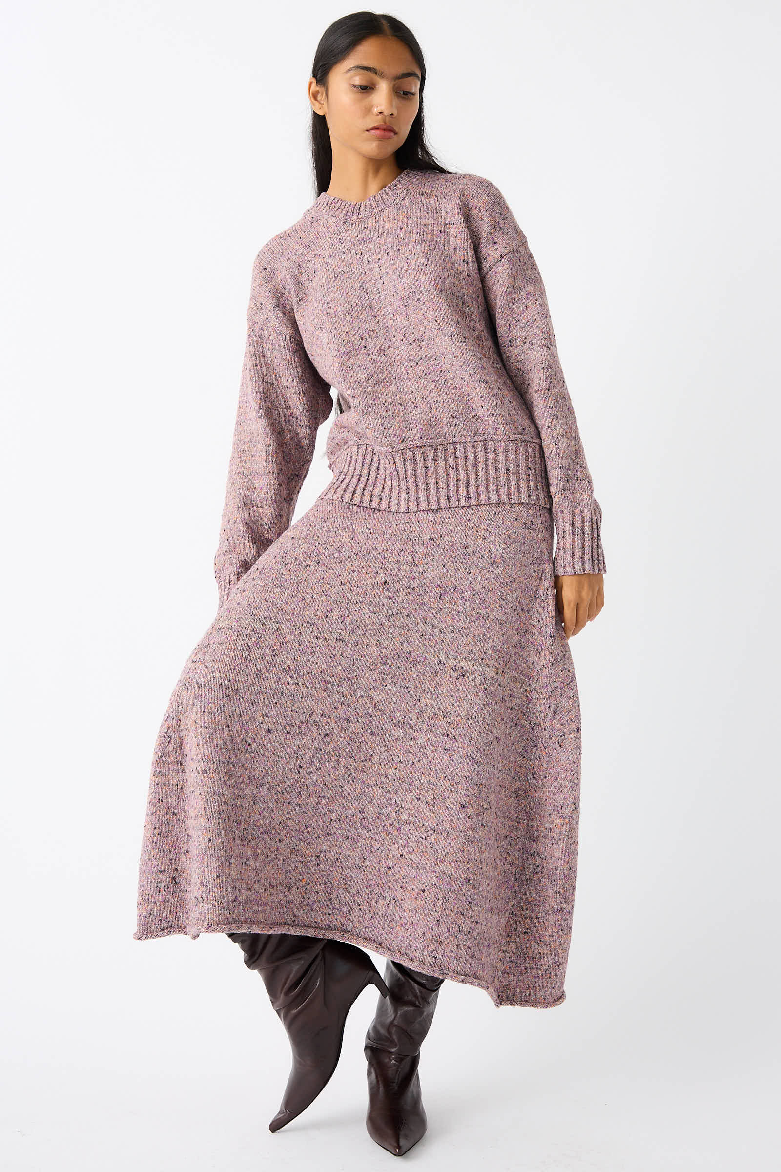 A woman stands wearing a matching purple sweater and the Rachel Comey Neps Tweed Knit Rapt Skirt in Violet, paired with knee-high brown boots, against a plain white background.