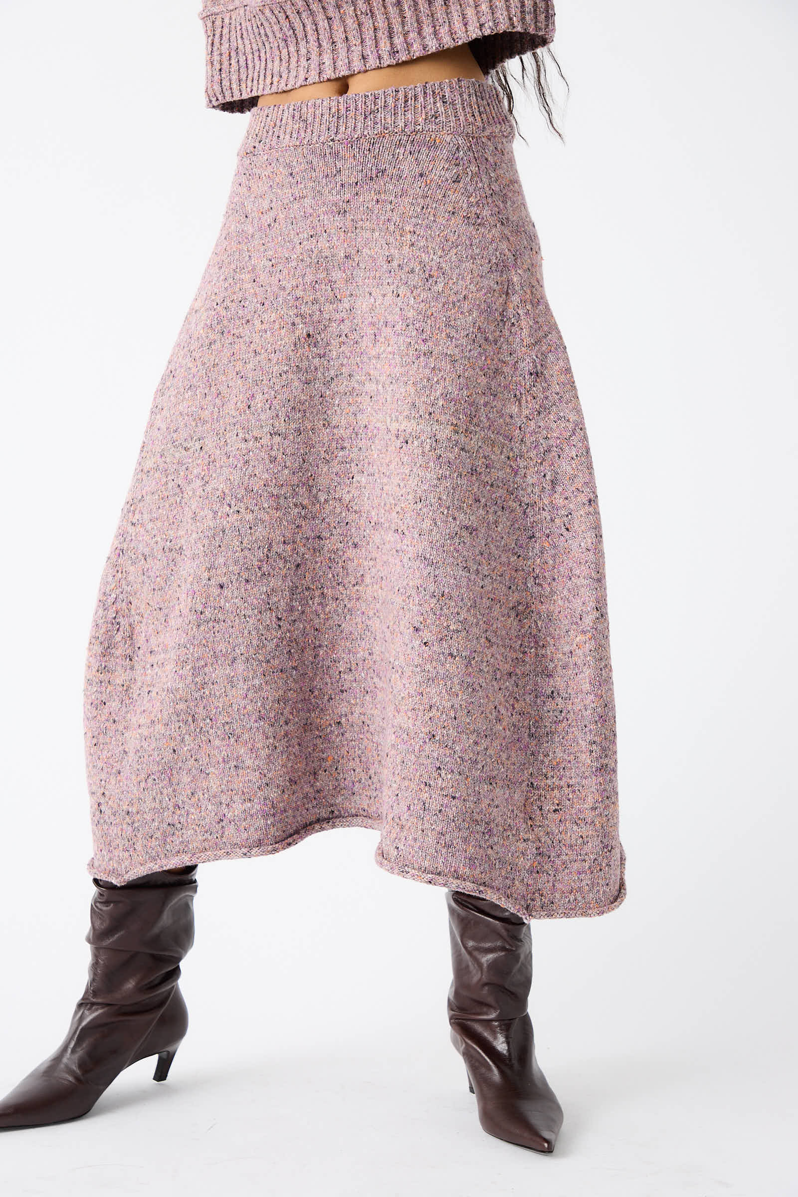 Person wearing a Neps Tweed Knit Rapt Skirt in Violet from Rachel Comey, brown boots, and a cropped pink knitted top, photographed from chin to boots against a plain background.