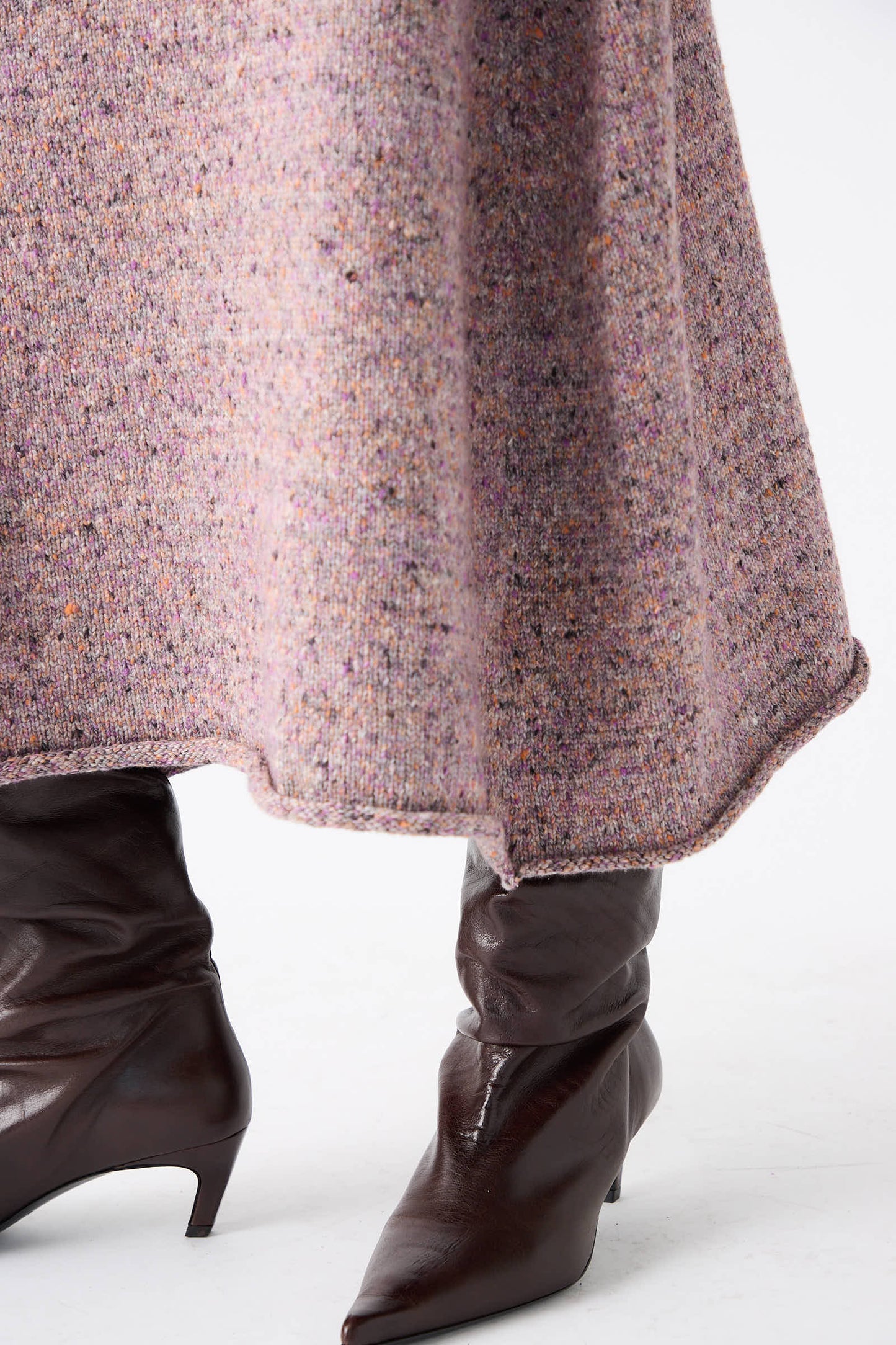 Close-up of a person wearing the Rachel Comey Neps Tweed Knit Rapt Skirt in Violet, featuring shades of pink and brown. The cocoon-shaped design pairs elegantly with dark brown, pointed-toe leather boots.