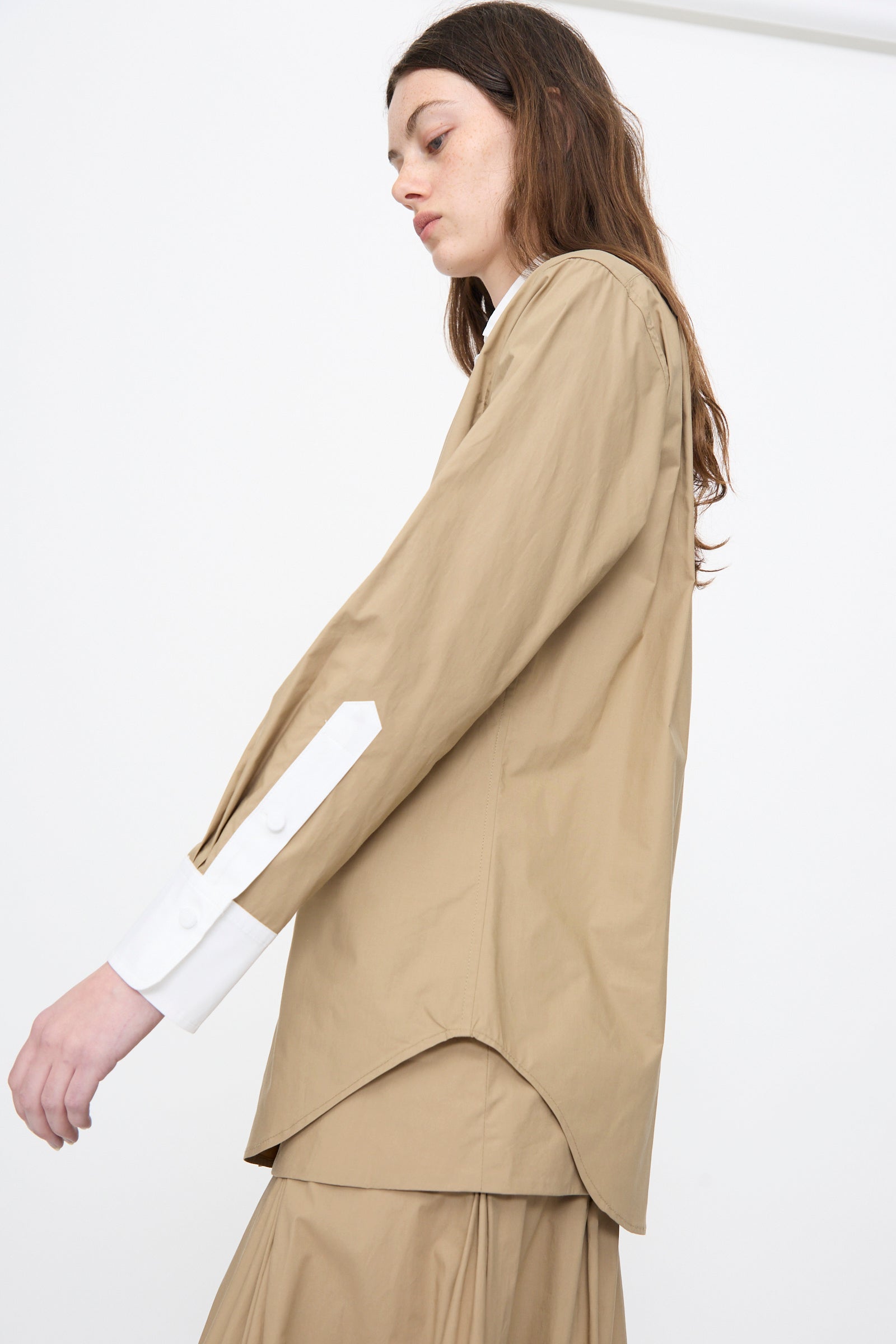 A person wearing the Rachel Comey Pierre Shirt in Khaki, featuring white cuffs, paired with a matching tan skirt, stands against a plain white background.