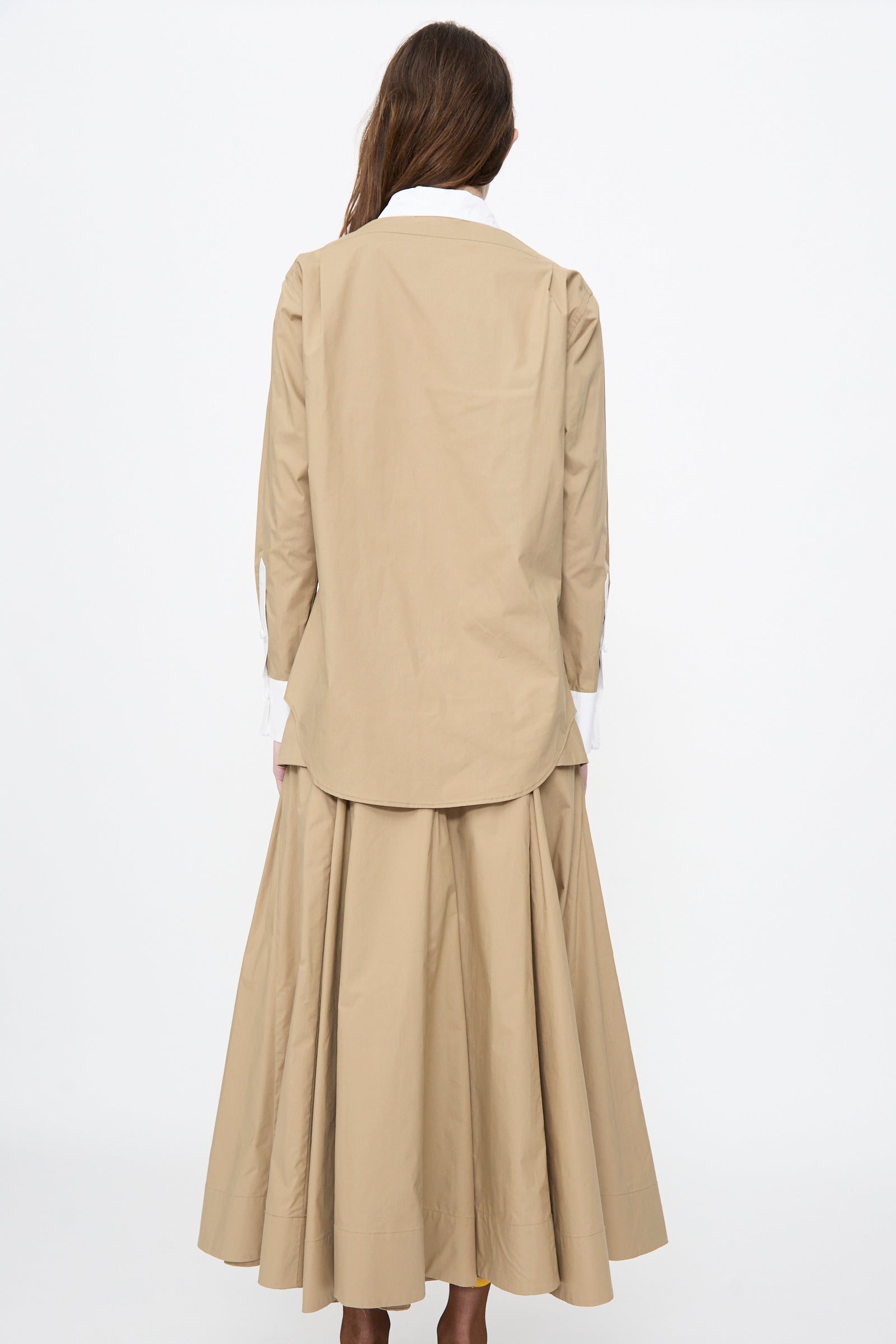 A woman stands facing away, wearing the Rachel Comey Pierre Shirt in Khaki with a white collar and cuffs, paired with a matching pleated, ankle-length skirt.