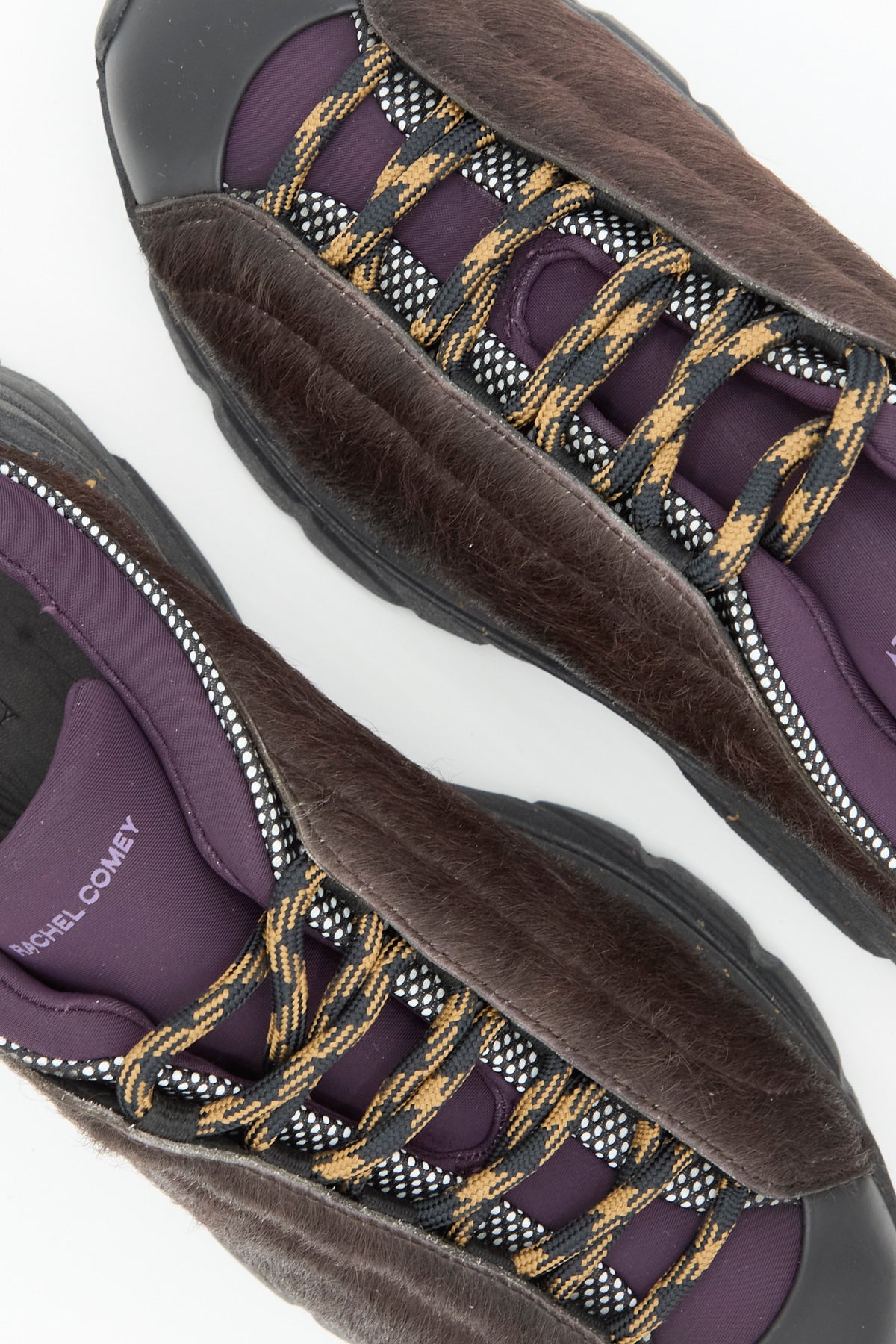 Close-up of two Rachel Comey Pilla Sneakers in Chestnut, featuring brown faux fur uppers, purple fabric accents, black soles, and yellow-and-black patterned laces—expertly made in Portugal.