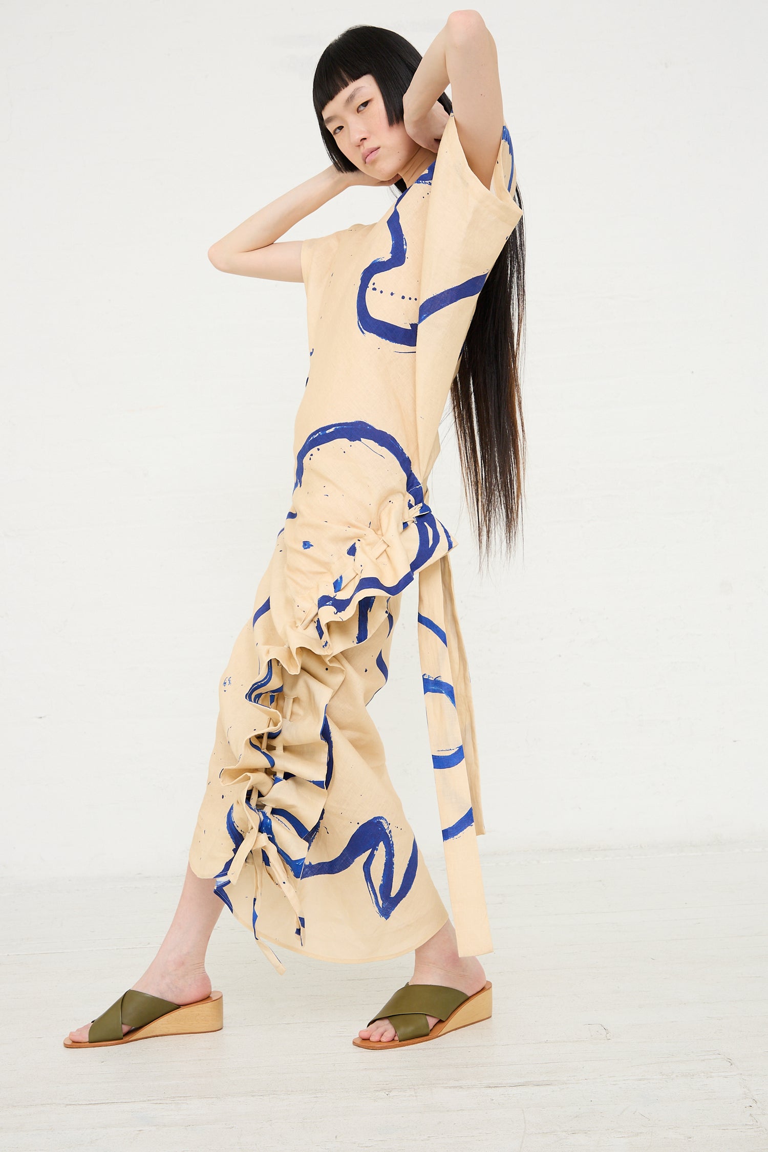 A woman in a unique avant-garde Rachel Comey Regent dress in blush, with abstract printed linen, posing against a white background.