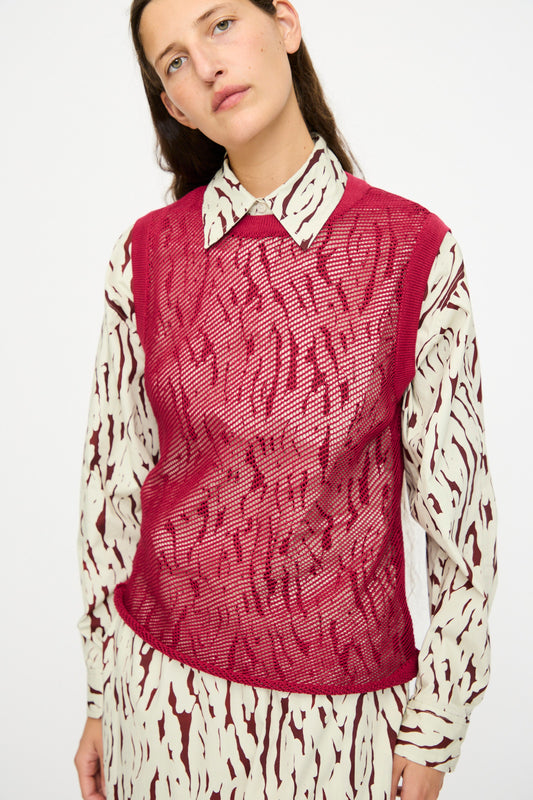 A person wears the Rachel Comey Rhett Tank in Deep Red, a sleeveless mesh vest, layered over a patterned cream and burgundy pima cotton shirt, standing against a plain light background.