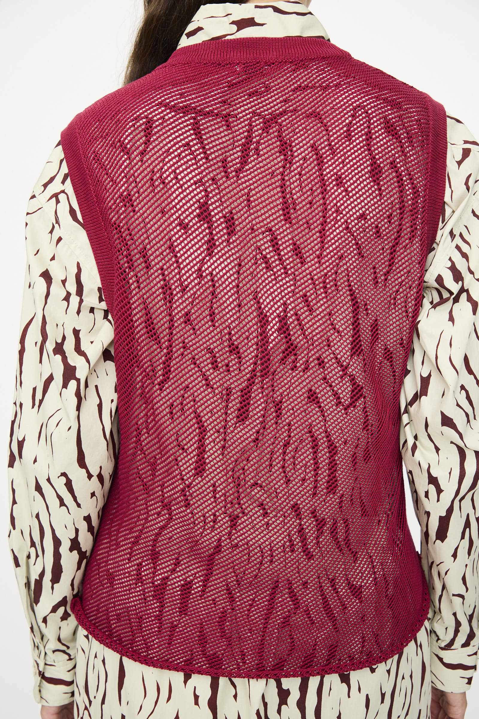 A person is seen from behind wearing the Rachel Comey Rhett Tank in Deep Red over a long-sleeve, abstract patterned shirt.
