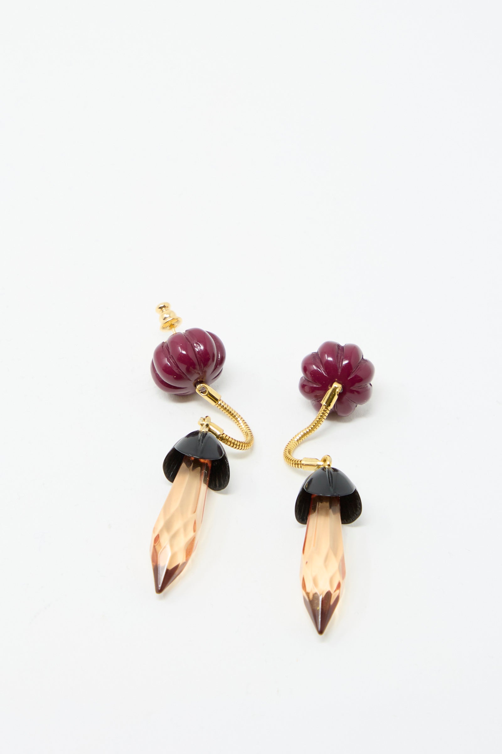 The Rosales Earring in Plum by Rachel Comey features flower-shaped stud tops, gold stems with intricate metal drop detailing, and crystal-like orange pendant ends, set against a white background.