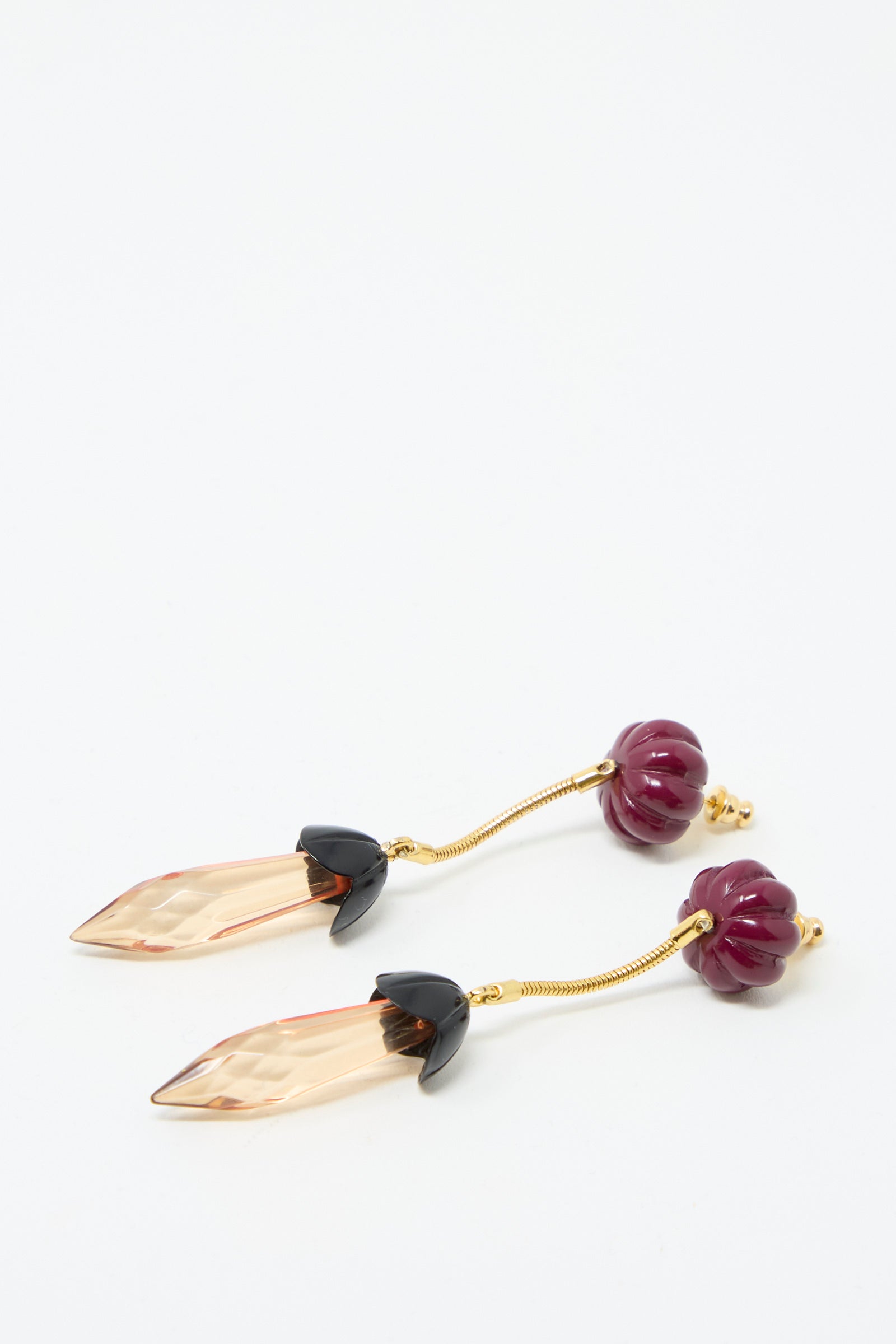 Rachel Comey's Rosales Earrings in Plum, featuring a flower-shaped stud design with gold-tone, pink crystal pendants, and purple beaded tops, are displayed on a white surface.