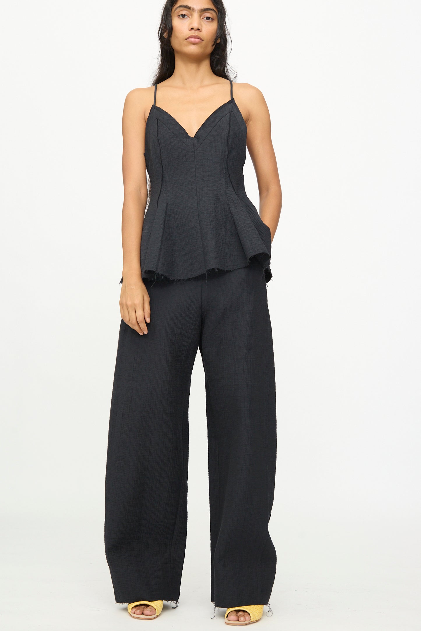 A woman wearing the Rachel Comey Tally Pant in Black, paired with a matching black sleeveless peplum top with spaghetti straps and high waist, wide leg silhouette, stands against a plain white background.