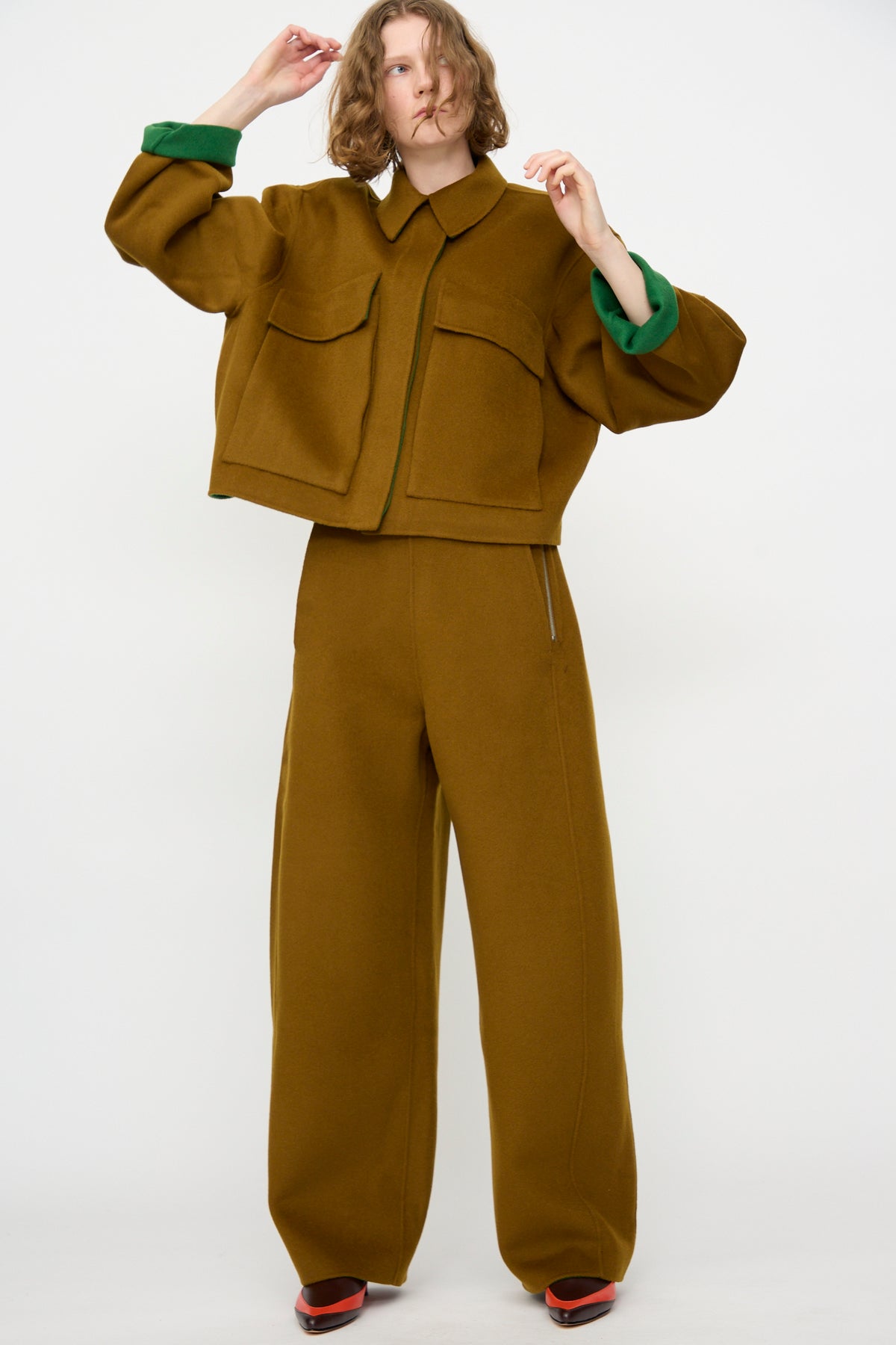 A person wearing the Rachel Comey Tally Pant in Bronze—relaxed fit, high-waist, wide-leg pants—paired with an oversized brown double-faced wool jacket with large front pockets, stands against a plain white background.