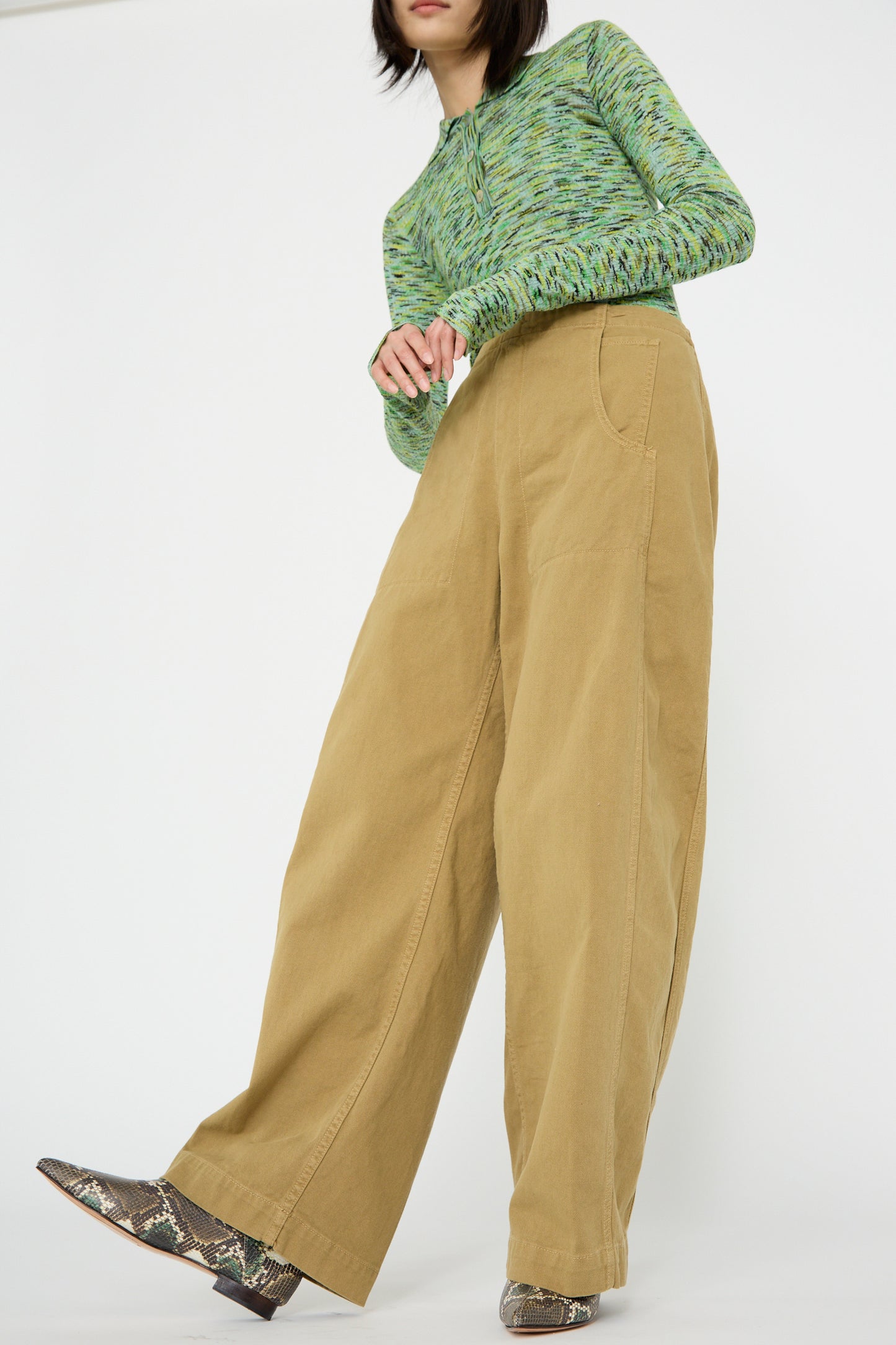 A person wearing a green long-sleeve top, Rachel Comey's Tany Pant in Olive, and patterned shoes stands against a plain background.