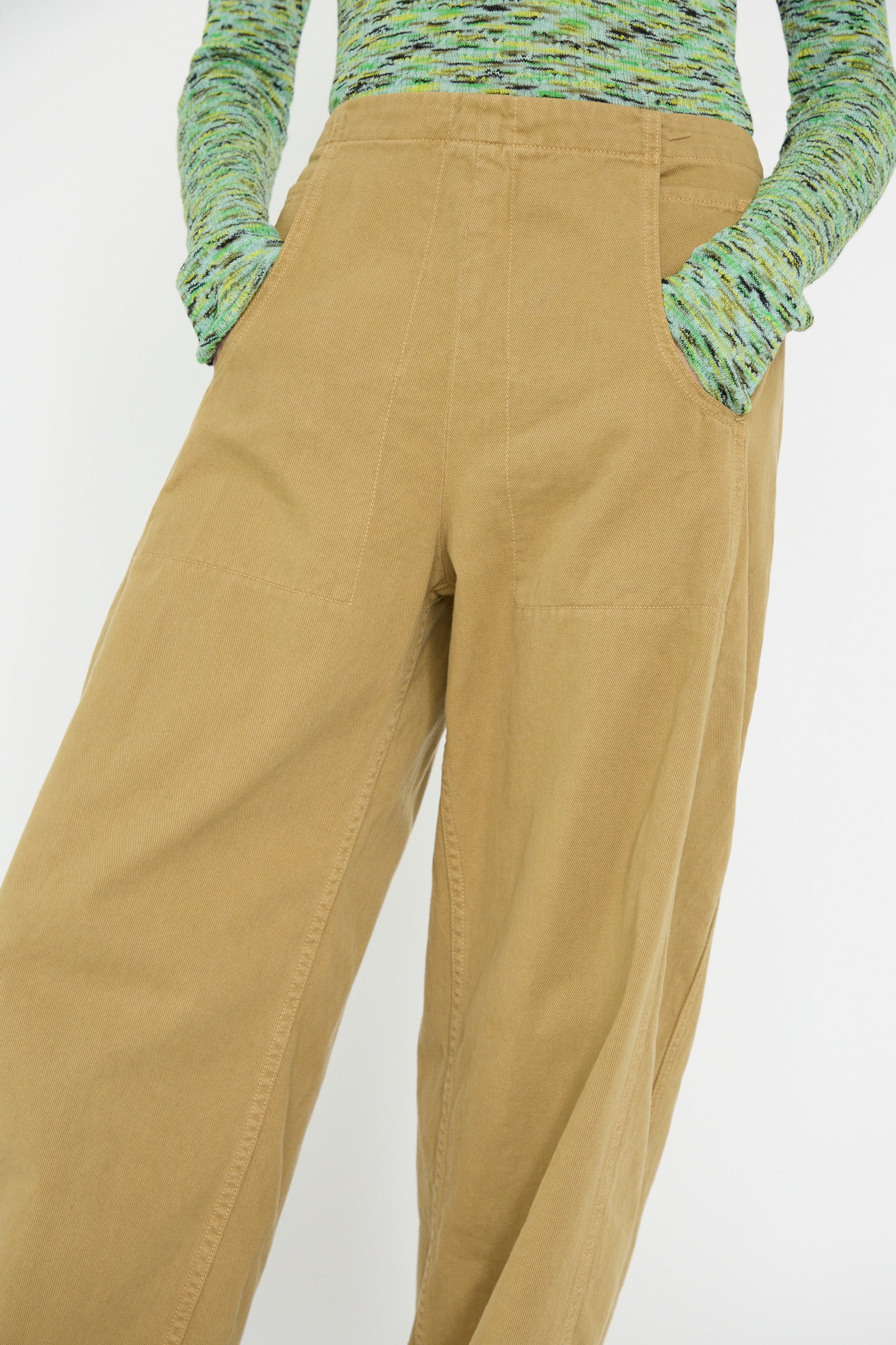 Someone wearing the Rachel Comey Tany Pant in Olive, a high-waisted, wide-leg design made from brushed bull denim, paired with a green-patterned long-sleeve top and hands in pockets.