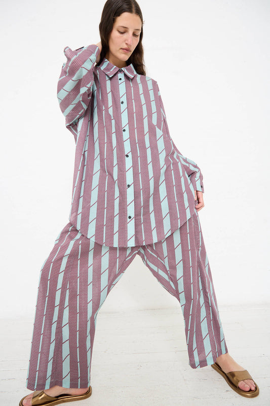 Person poses in a matching oversized shirt and Rachel Comey Tess Pant in Aqua with vertical stripes in purple and light blue tones, made from organic cotton, wearing brown sandals against a plain white background.