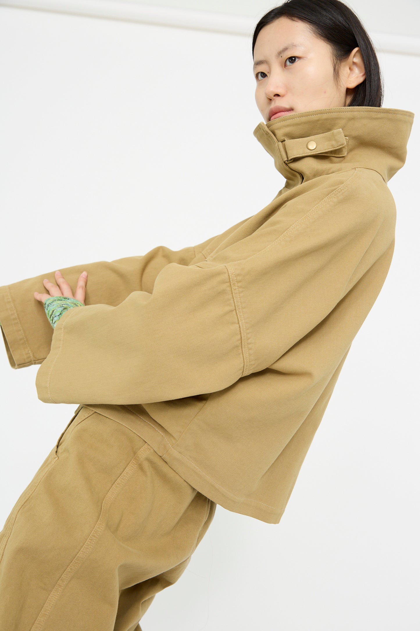 A person stands sideways against a plain background, wearing the Rachel Comey Vansire Jacket in Olive with matching pants. 