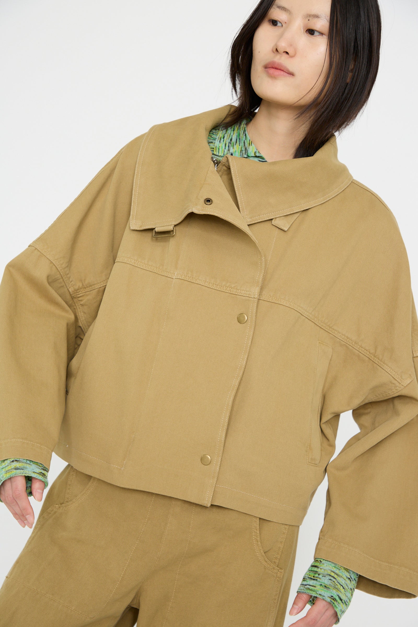 Against a plain backdrop, a person wears Rachel Comey's Vansire Jacket in Olive, arms down on either side. 