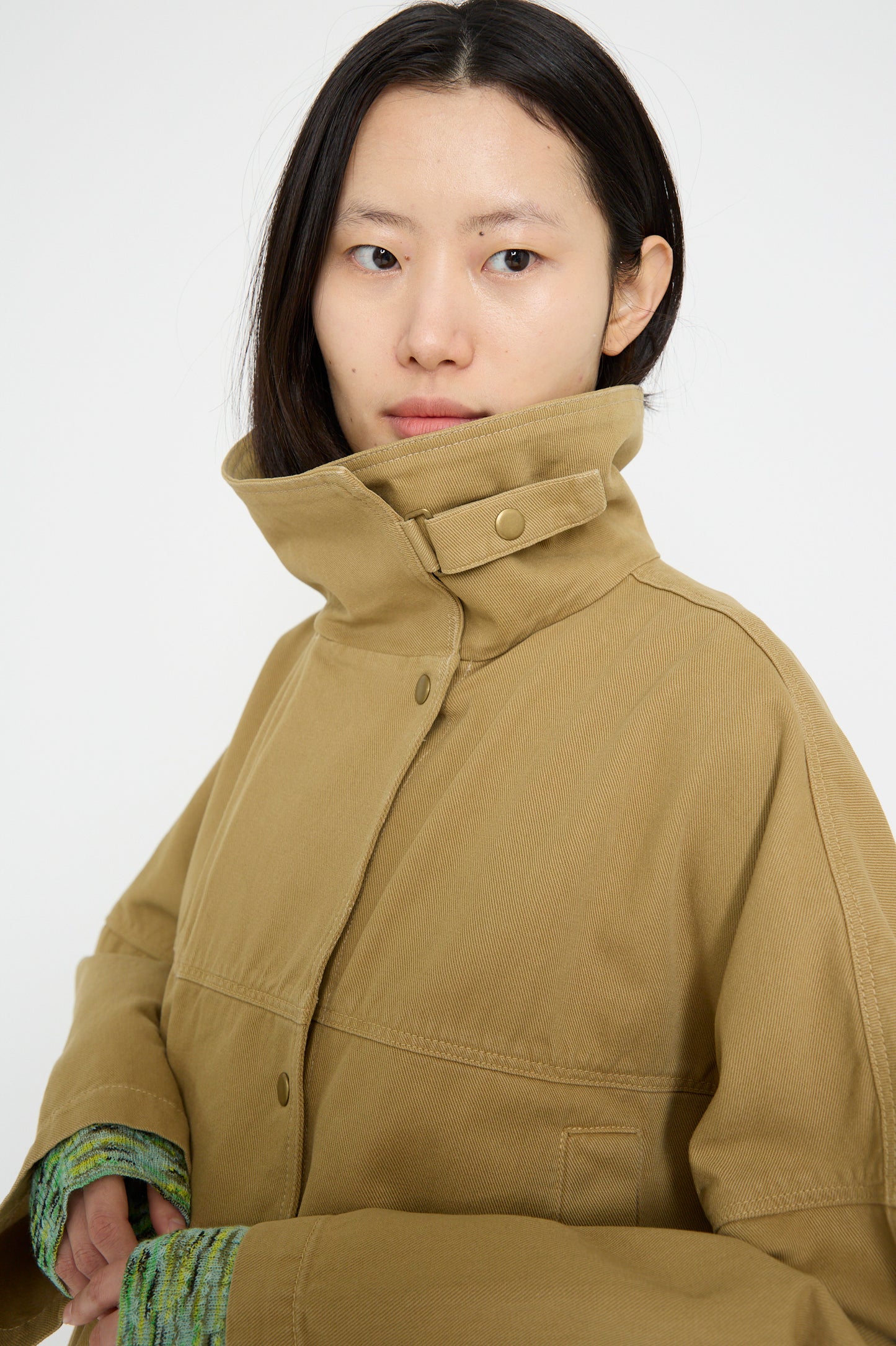 The person is wearing a Vansire Jacket in Olive by Rachel Comey, featuring a boxy fit with a high collar, looking to the side against a plain background.