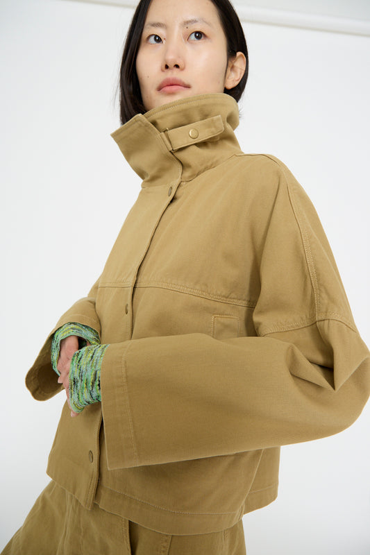 Wearing the Rachel Comey Vansire Jacket in Olive, featuring a boxy fit with a high collar and bell-shaped sleeves over a textured green garment, the person looks upward and effortlessly captures attention.