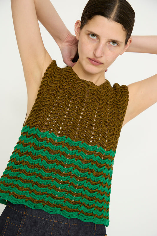 A person in the Wavy Crochet Bonita Top by Rachel Comey, featuring a sleeveless knit design in Olive Multi, stands with raised arms and looks upward against a white background.