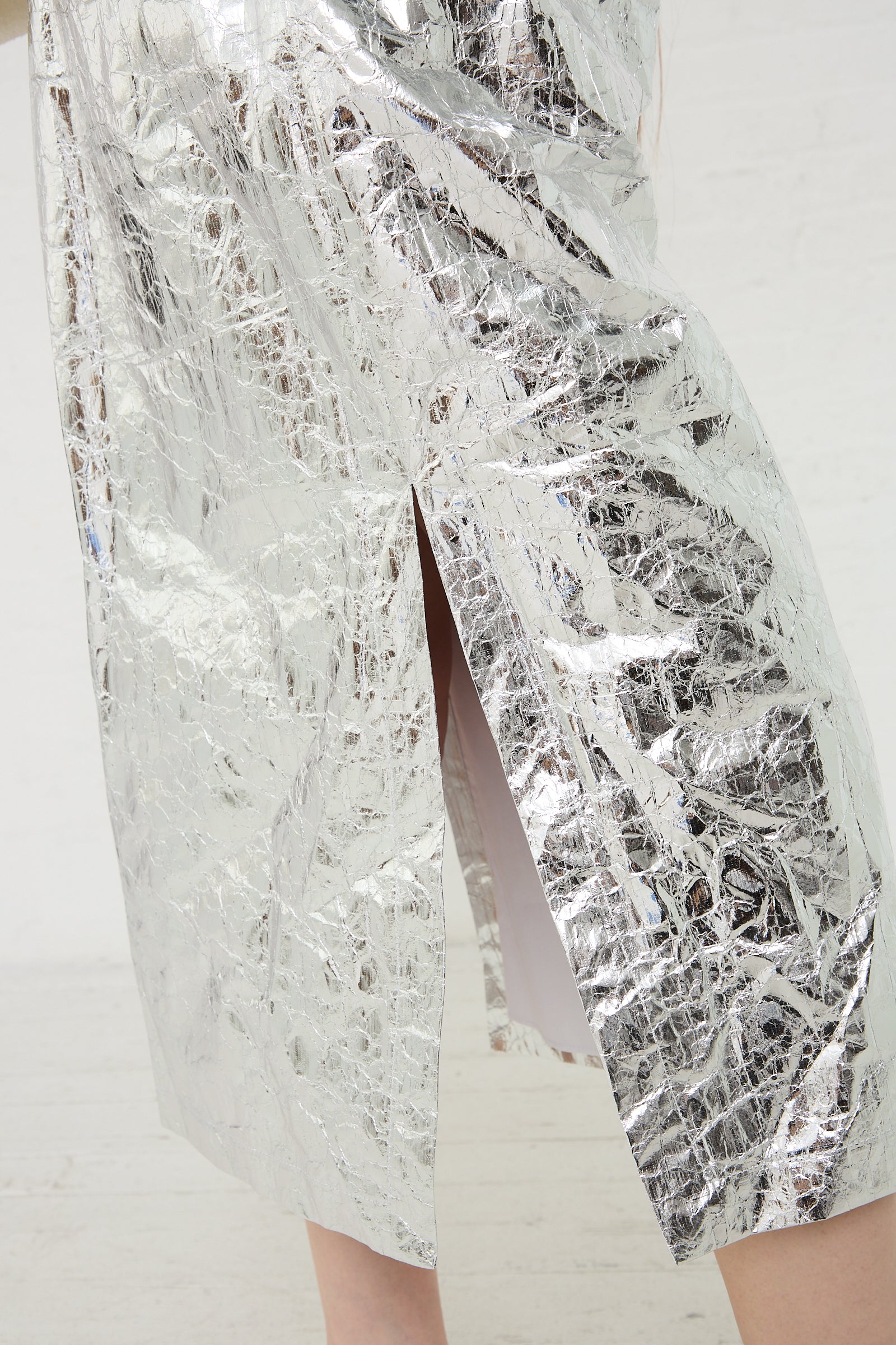 A close-up of a Rachel Comey Mott Skirt in Silver, a metallic silver, textured fabric with a slit.
