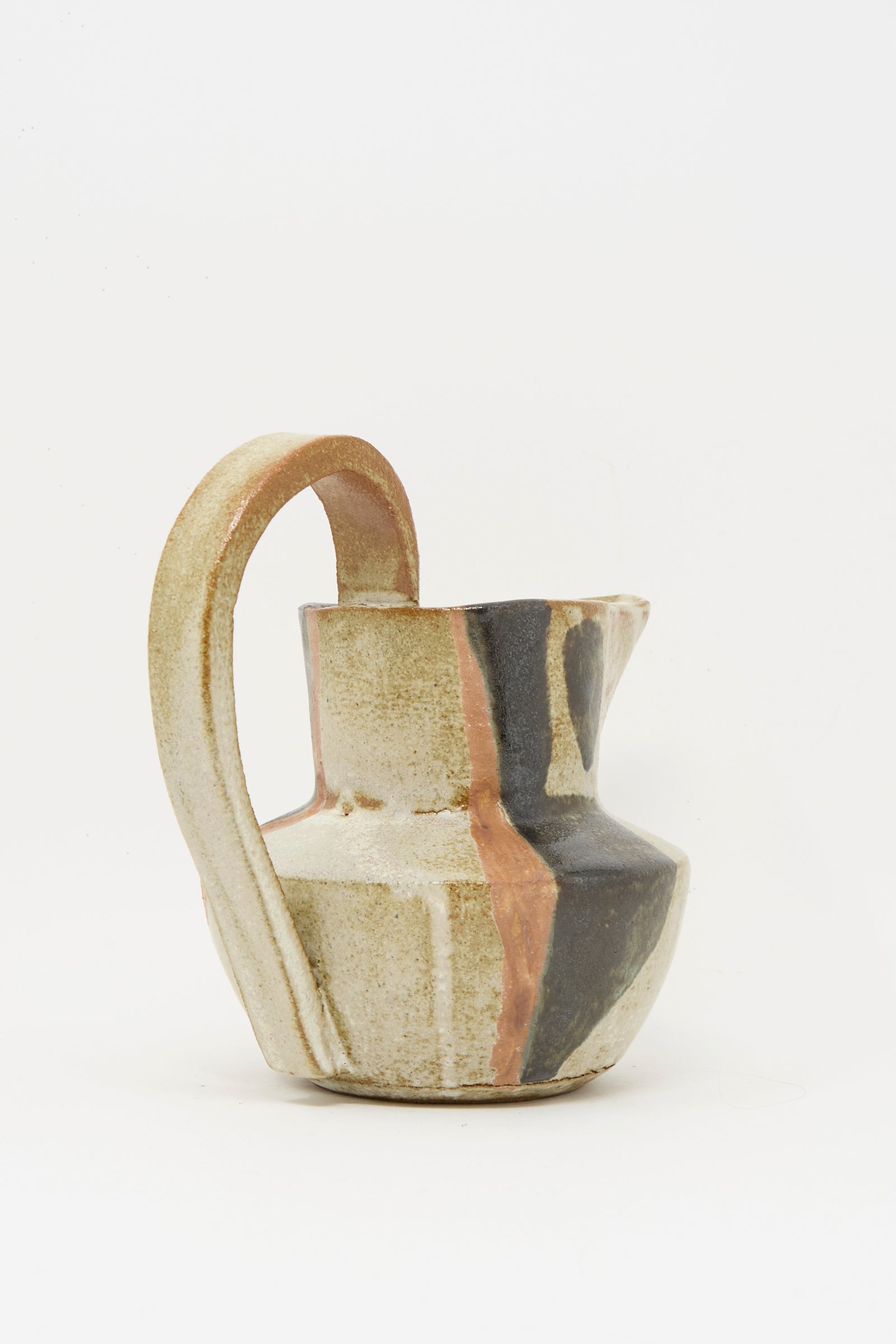 The Rachel Craven Drawn Pitcher in Creme is handmade with a wide handle, features an abstract pattern in beige, black, and muted orange tones, and is finished with a mineral glaze, photographed against a plain white background.