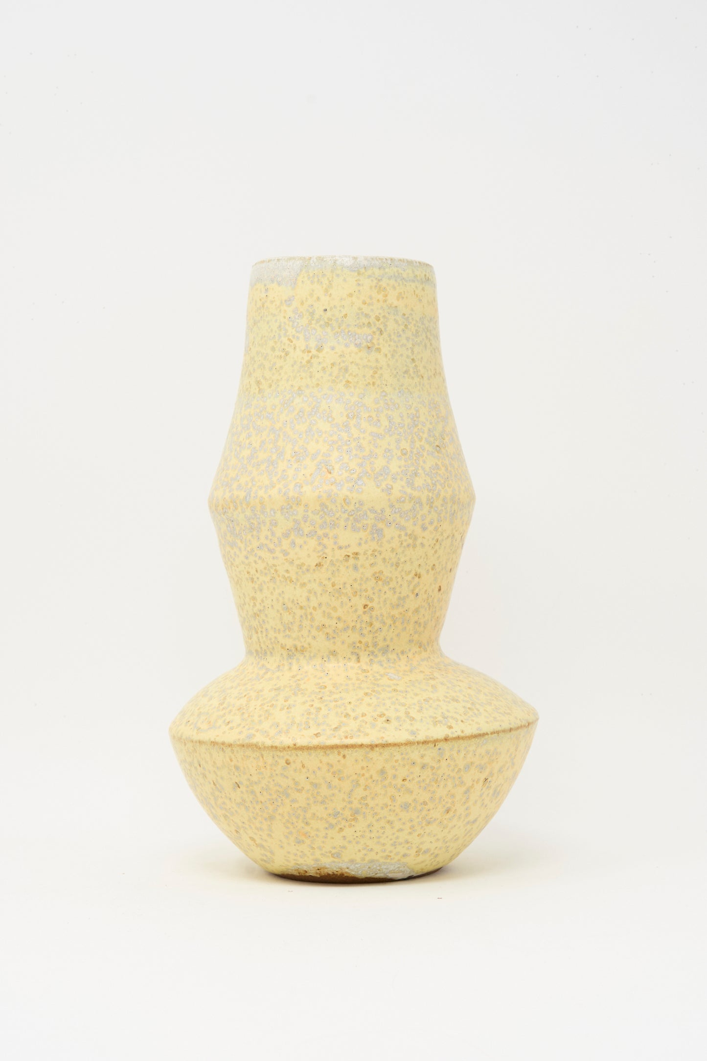 The Rachel Craven Shaped Vase in Eggshell Speckle features a light yellow, textured handmade clay design with a narrow middle and wider top and bottom, shown against a plain white background.