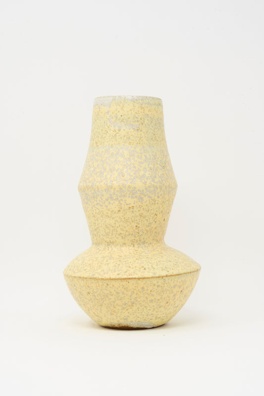 The Rachel Craven Shaped Vase in Eggshell Speckle features a light yellow, textured handmade clay design with a narrow middle and wider top and bottom, shown against a plain white background.